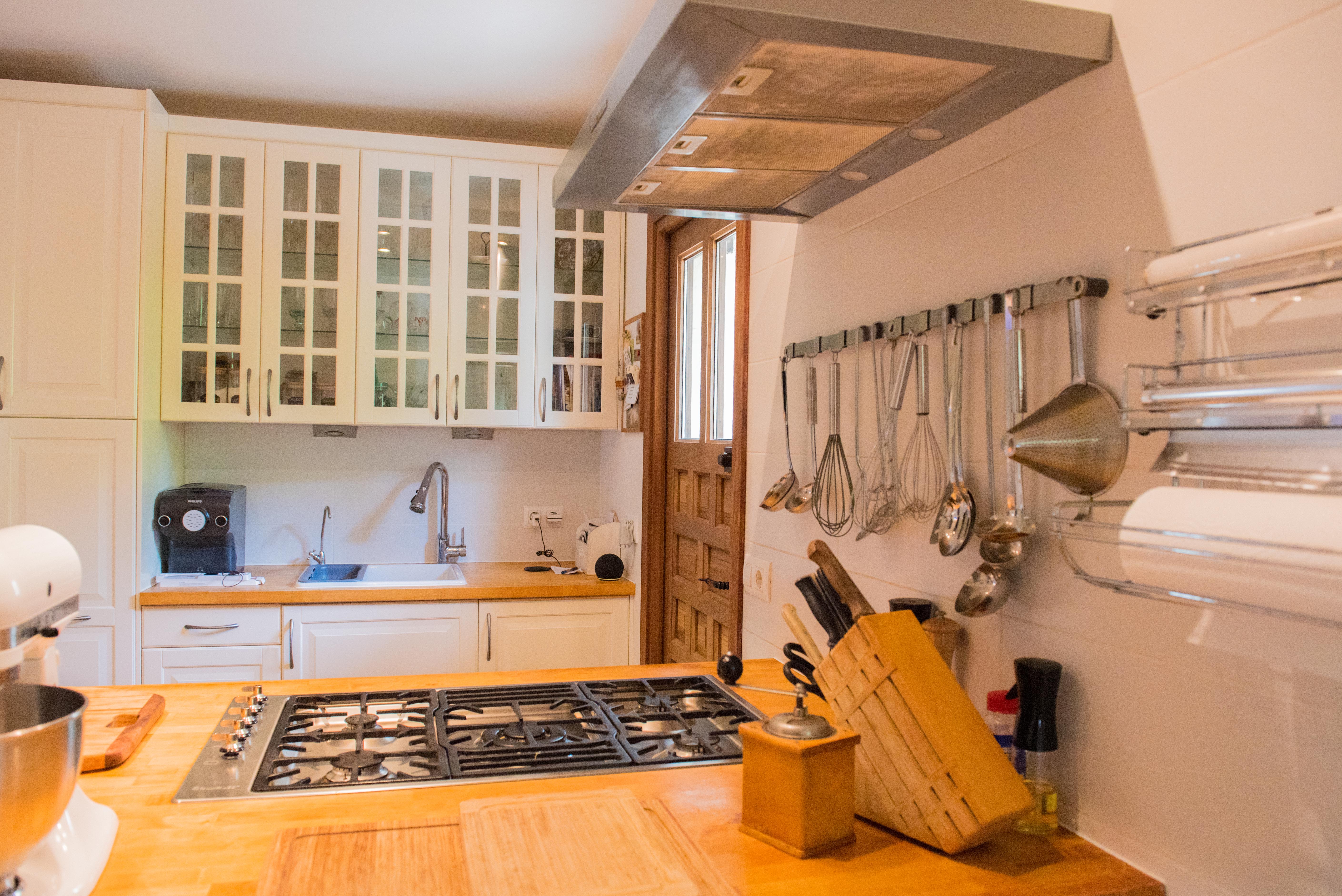 Functional kitchen featuring wooden countertops, an integrated gas cooktop, and white cabinetry with glass-front uppers. Includes a prep area with hanging utensils and a wood door.