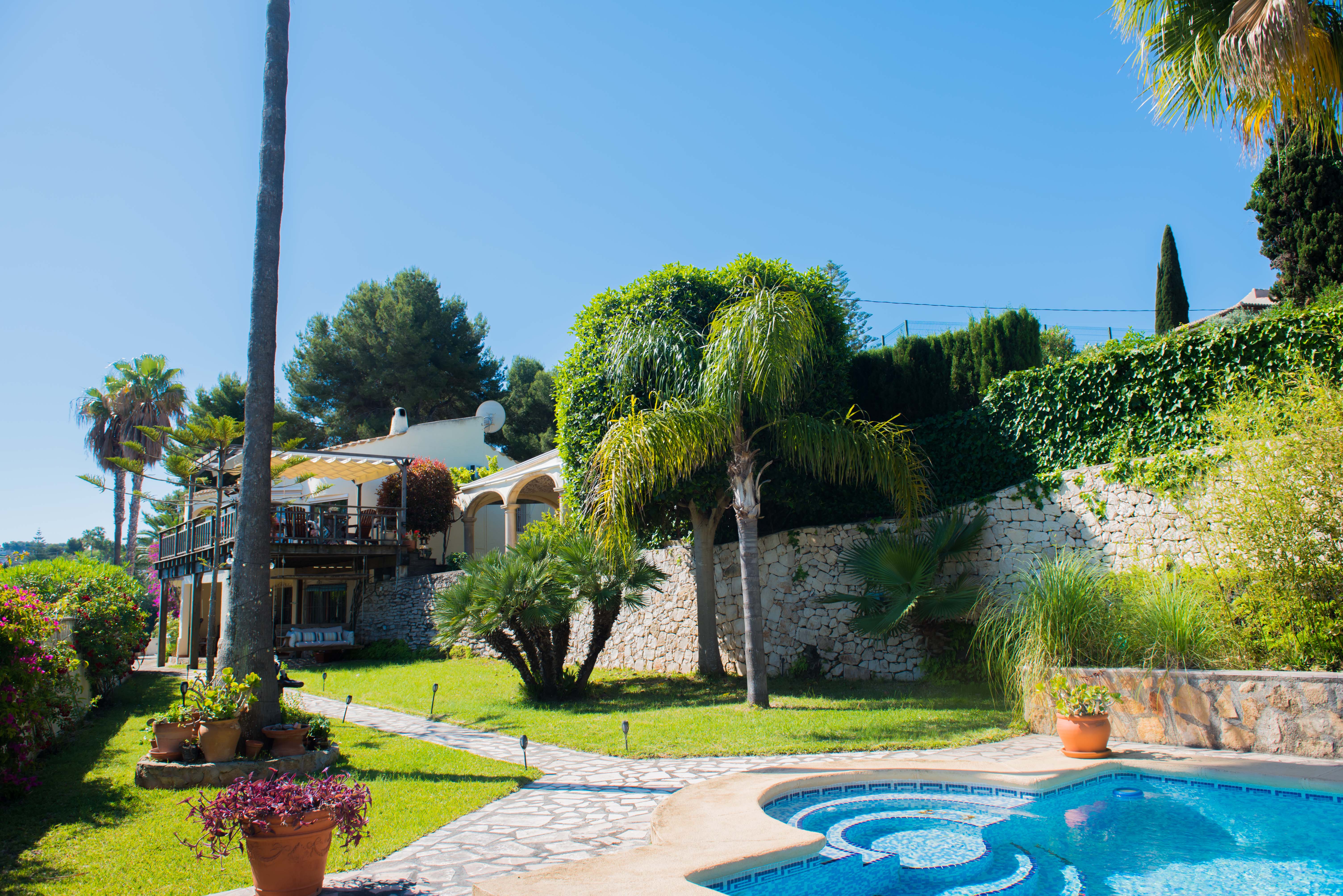 Garden view with a blue mosaic pool and a stone path leading to the Mediterranean-style villa. Garden view with a blue mosaic pool and a stone path leading to the Mediterranean-style villa.