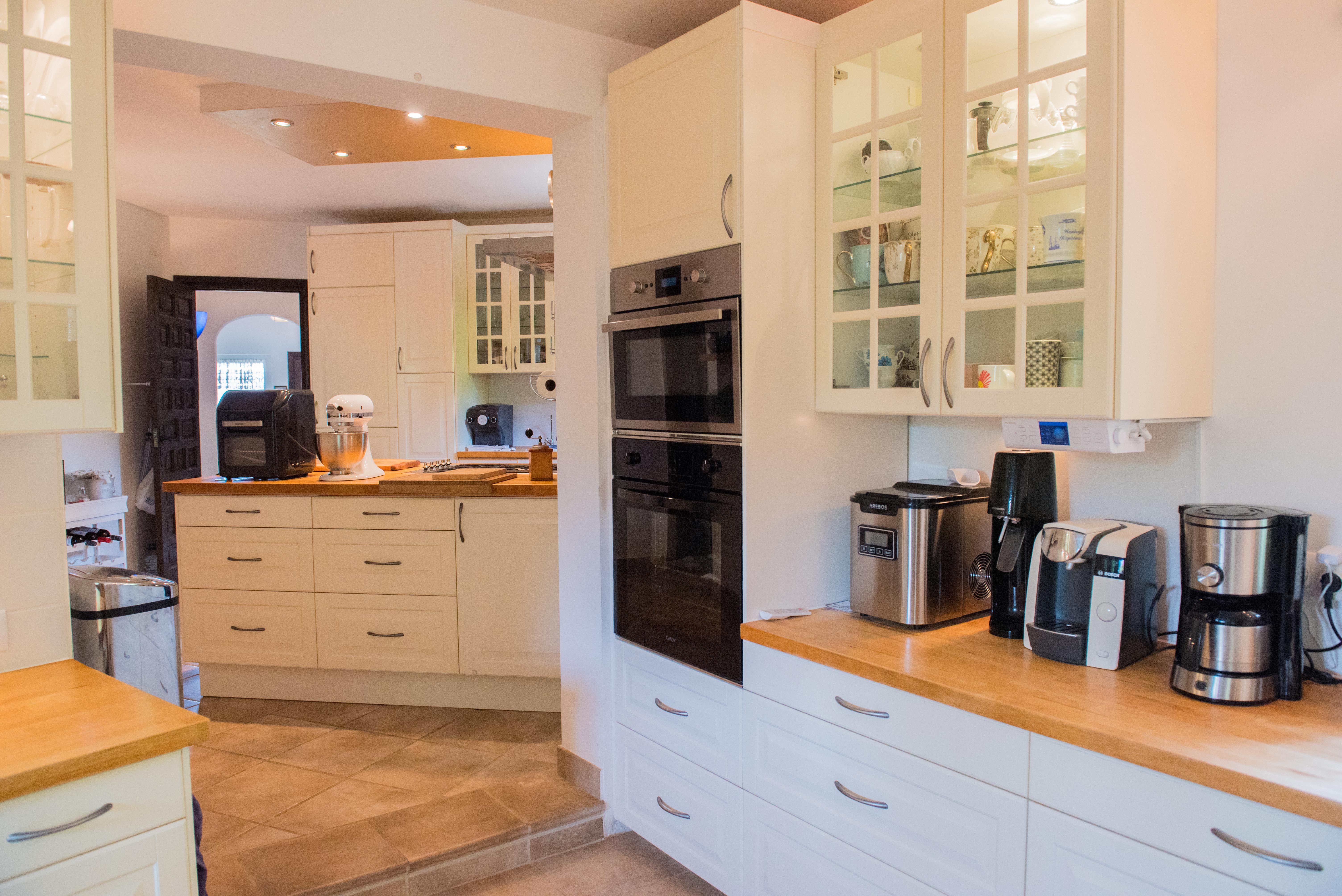 Kitchen featuring natural wood countertops, cream cabinetry, and integrated double ovens. Includes glass-front upper cabinets, recessed lighting, and tiled flooring.