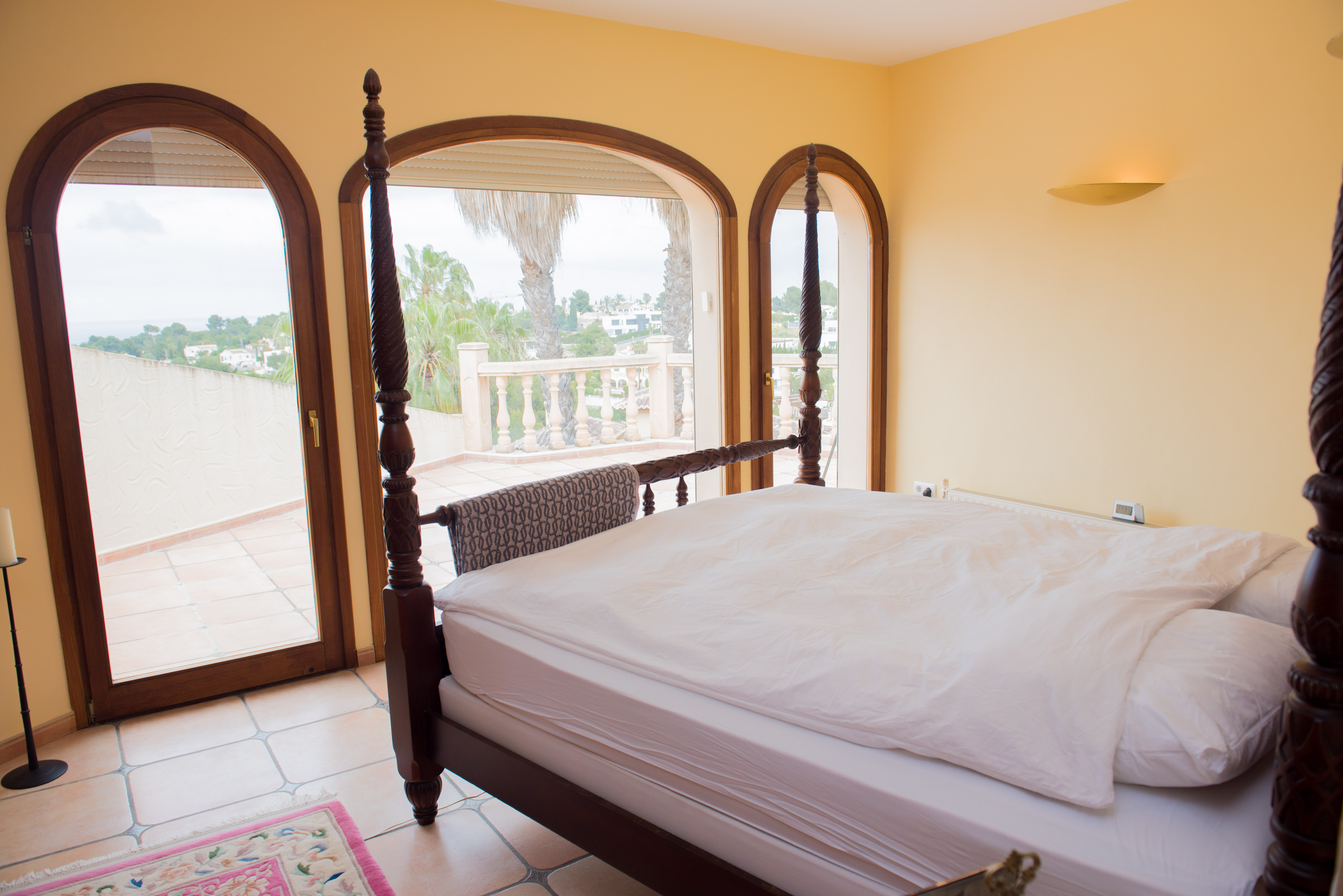 Master suite featuring a dark wood four-poster bed and arched glass doors opening onto a private terrace with Mediterranean views.