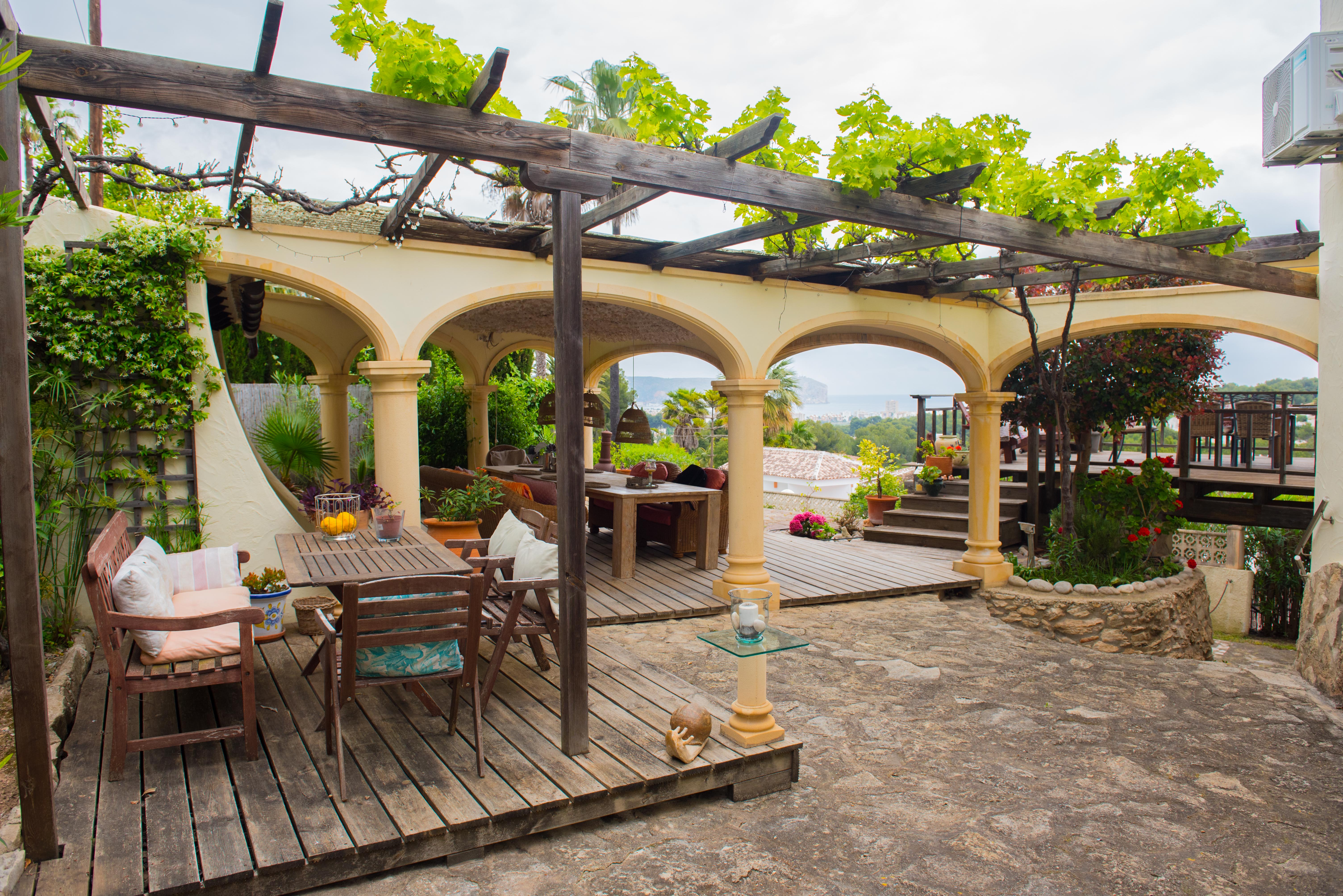 Outdoor terrace featuring a wooden pergola with climbing vines, timber decking, and an arched porch offering expansive sea and coastal views.