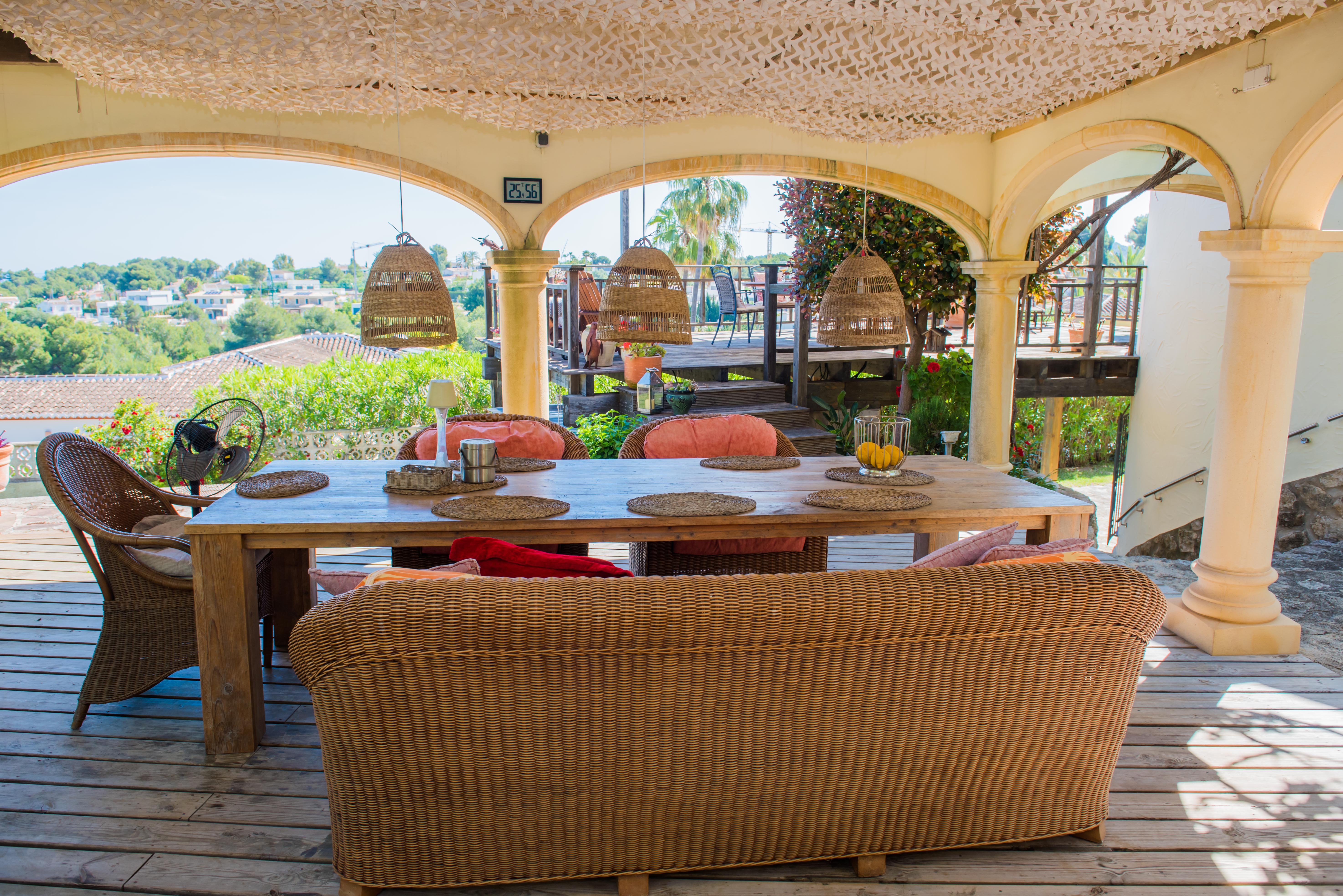 Porch with rustic wood table and wicker seating, illuminated by wicker pendant lamps, overlooking the landscape. Porch with rustic wood table and wicker seating, illuminated by wicker pendant lamps, overlooking the landscape.