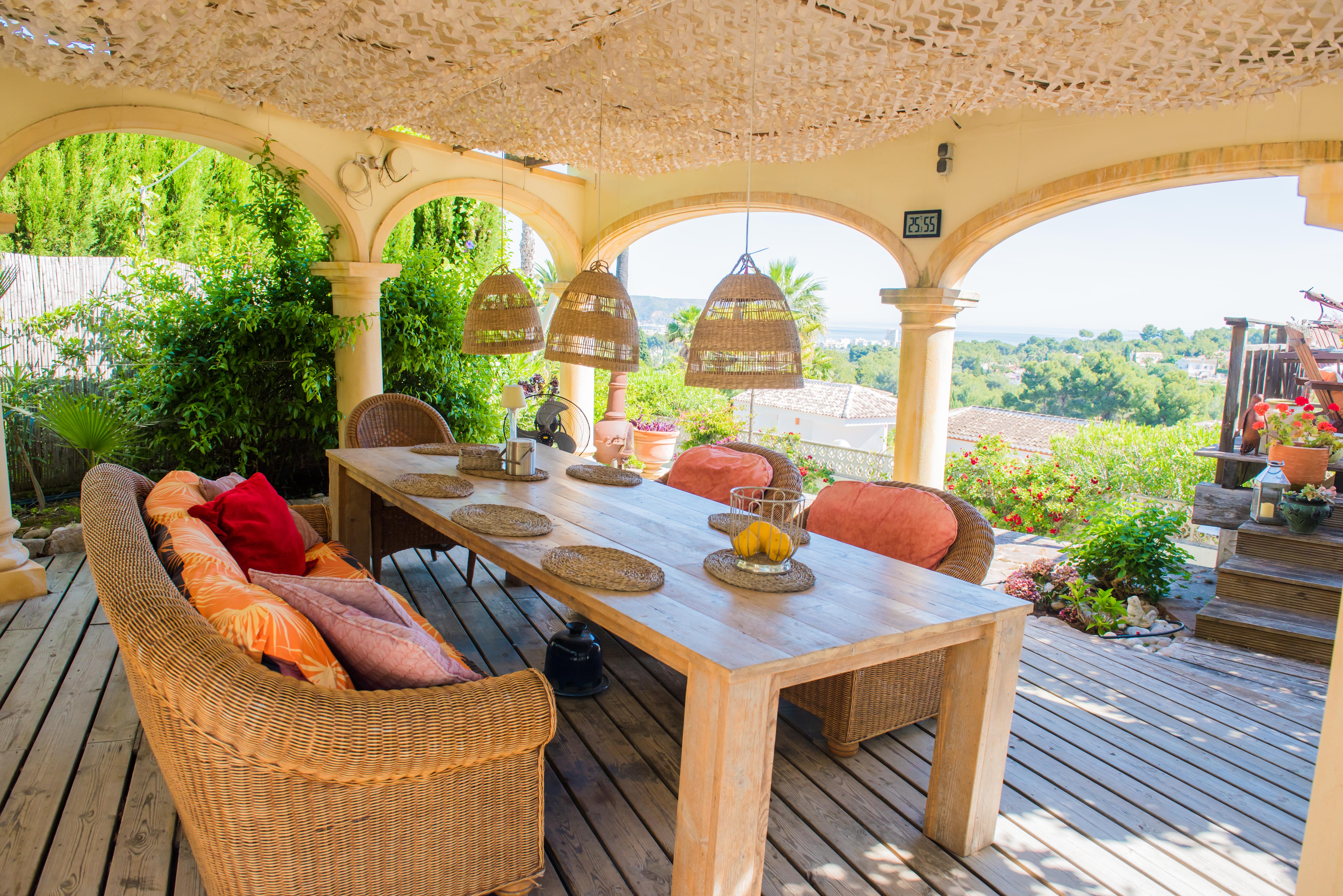 Porch with rustic wood table and wicker seating, offering panoramic views of the garden and the Mediterranean Sea. Porch with rustic wood table and wicker seating, offering panoramic views of the garden and the Mediterranean Sea.