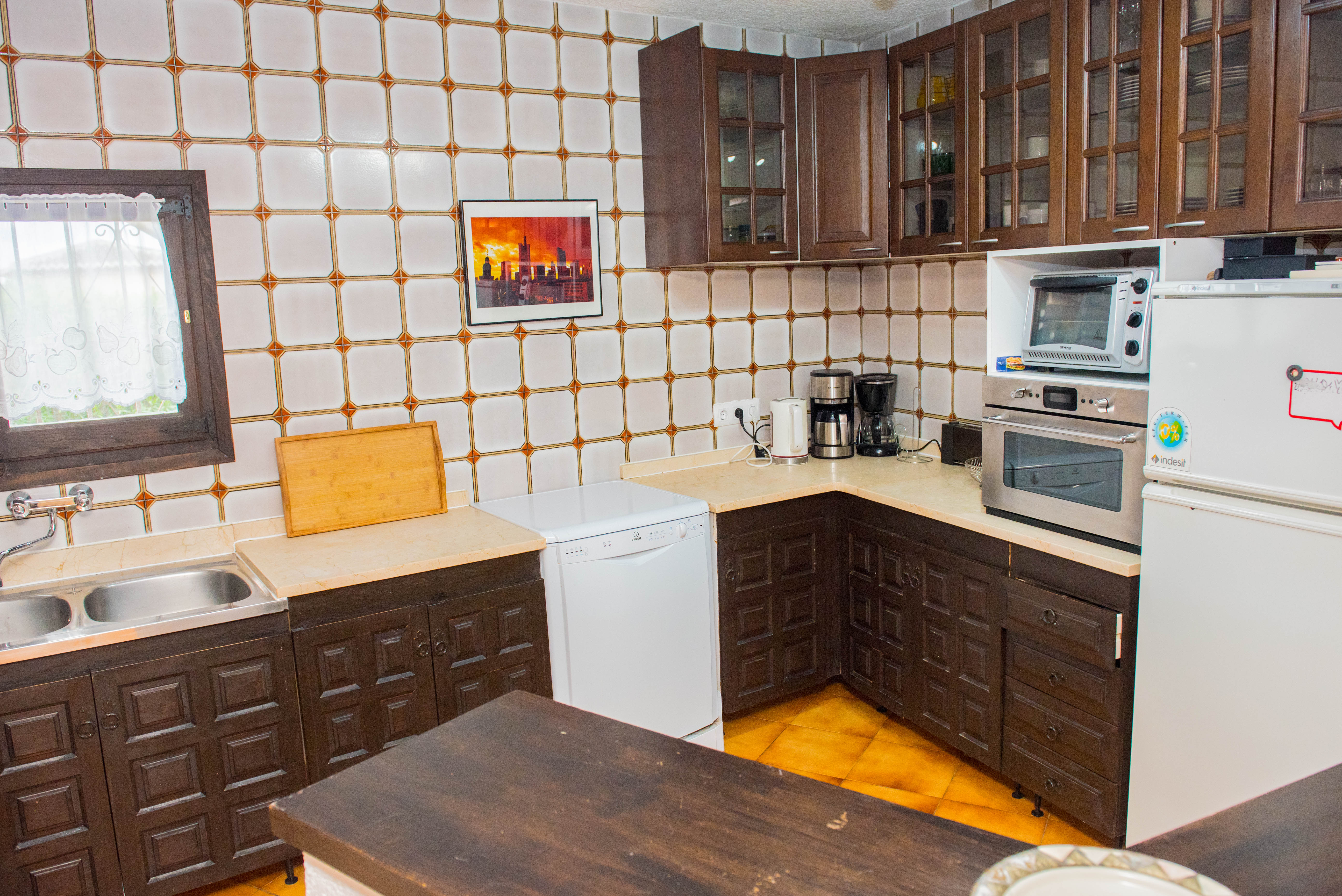 Rustic kitchen featuring dark carved wood cabinetry, cream countertops, and patterned wall tiles. Includes a white dishwasher, refrigerator, and built-in oven.