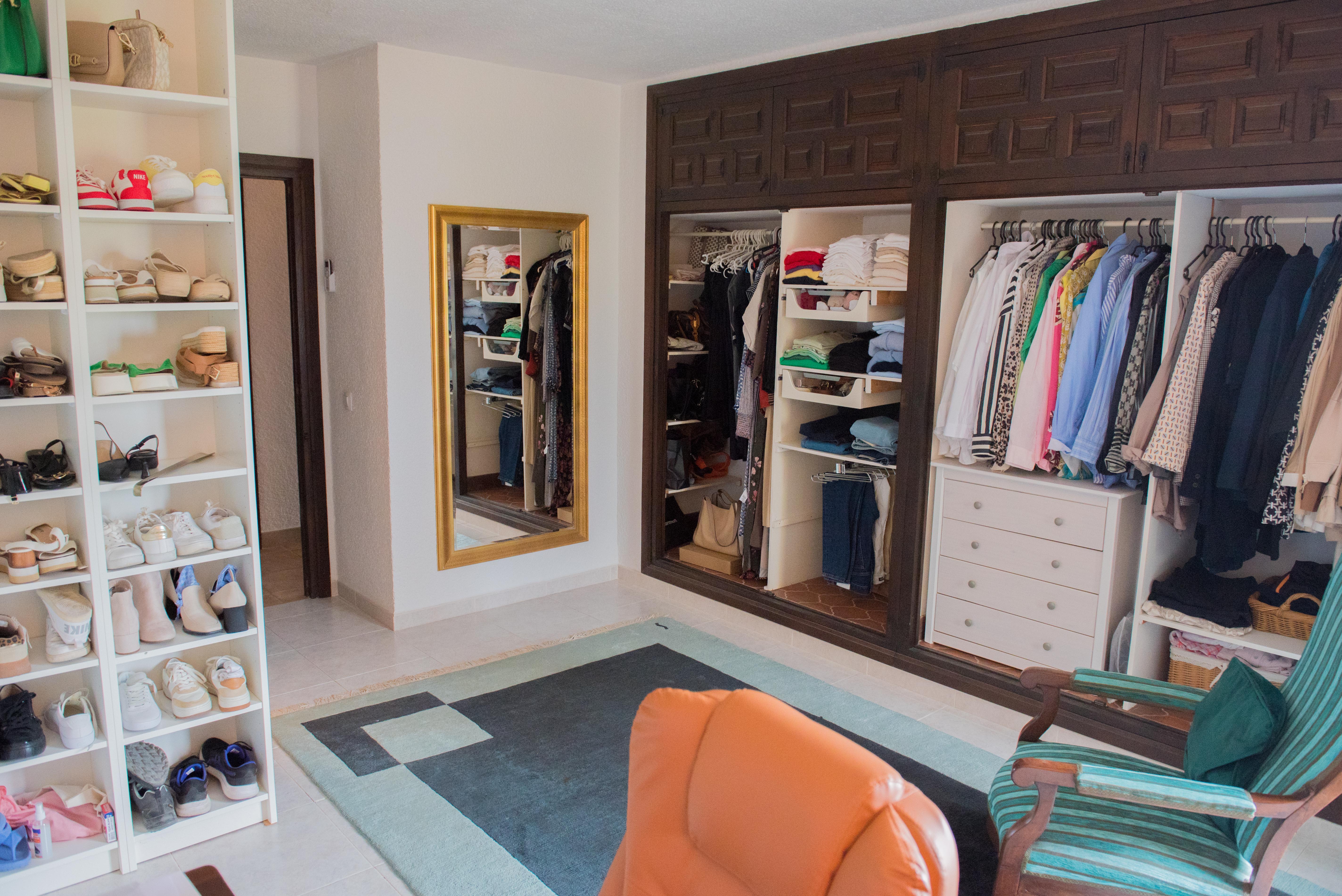 Spacious dressing room featuring dark wood built-in wardrobes, white shoe shelving, a gold-framed full-length mirror, and a seating area with a geometric rug.
