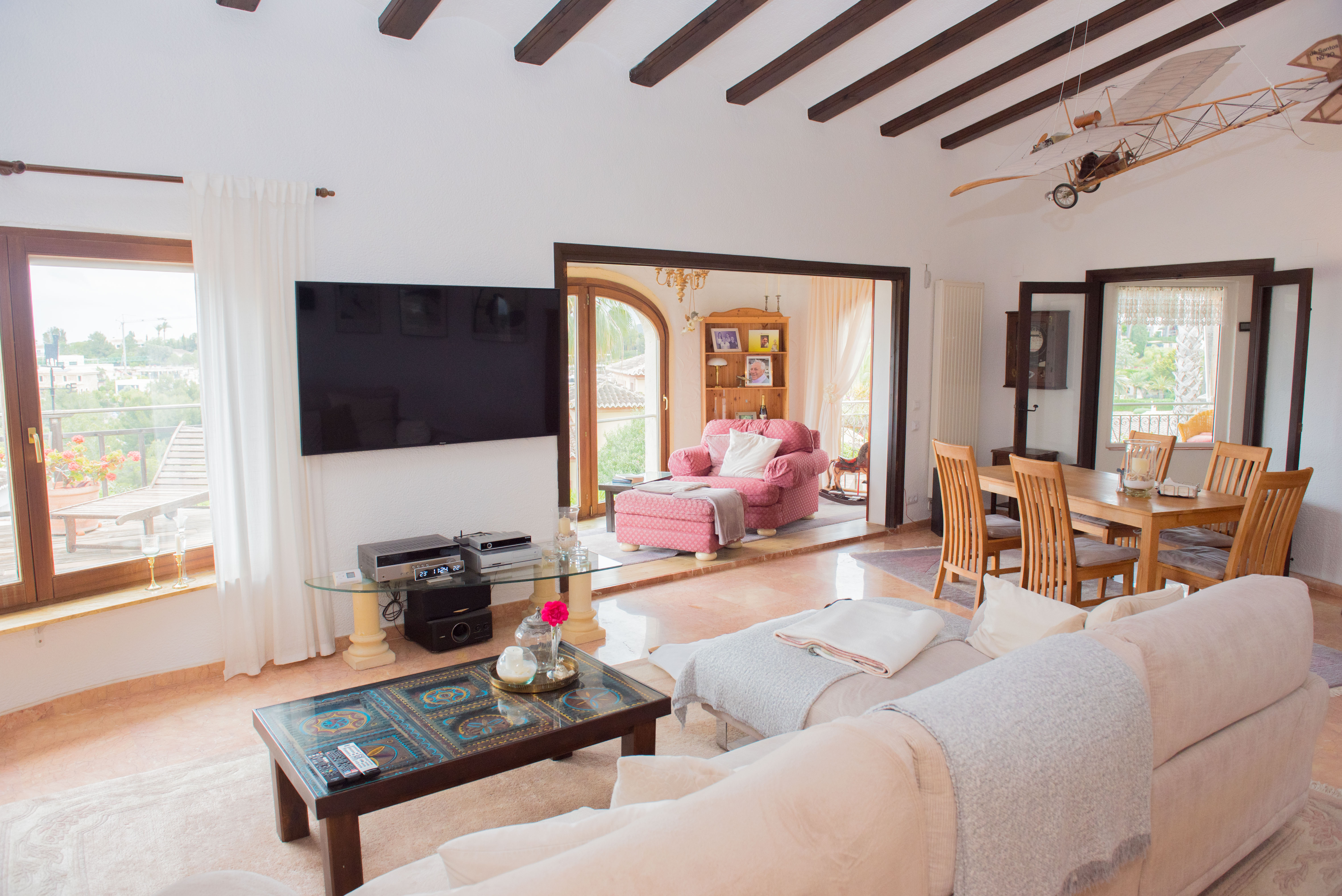 Spacious living and dining area featuring exposed dark wood ceiling beams, marble flooring, and direct access to a terrace with panoramic coastal views.