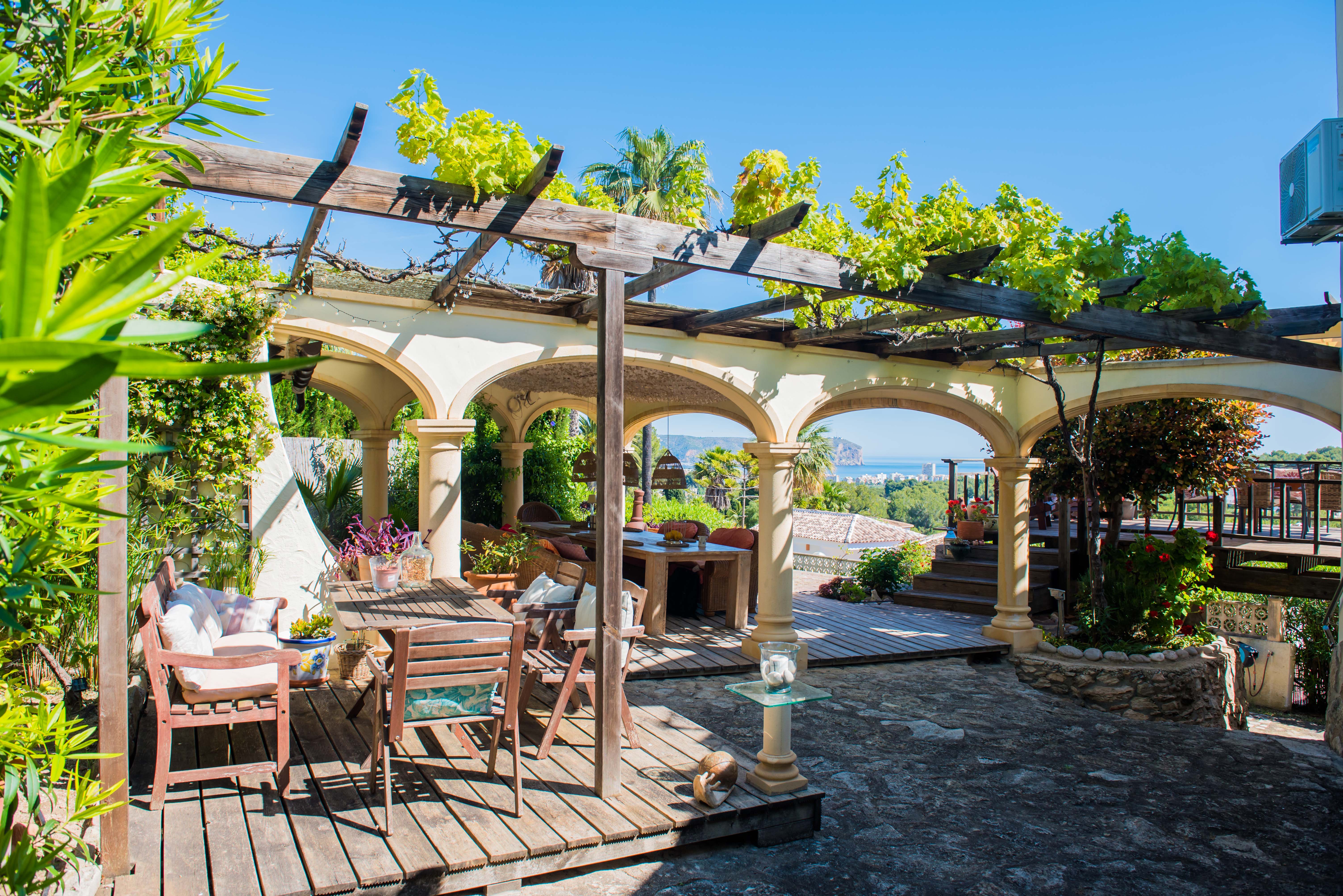 Terrace with a wooden pergola covered in greenery and stone arches overlooking the Mediterranean Sea. Terrace with a wooden pergola covered in greenery and stone arches overlooking the Mediterranean Sea.