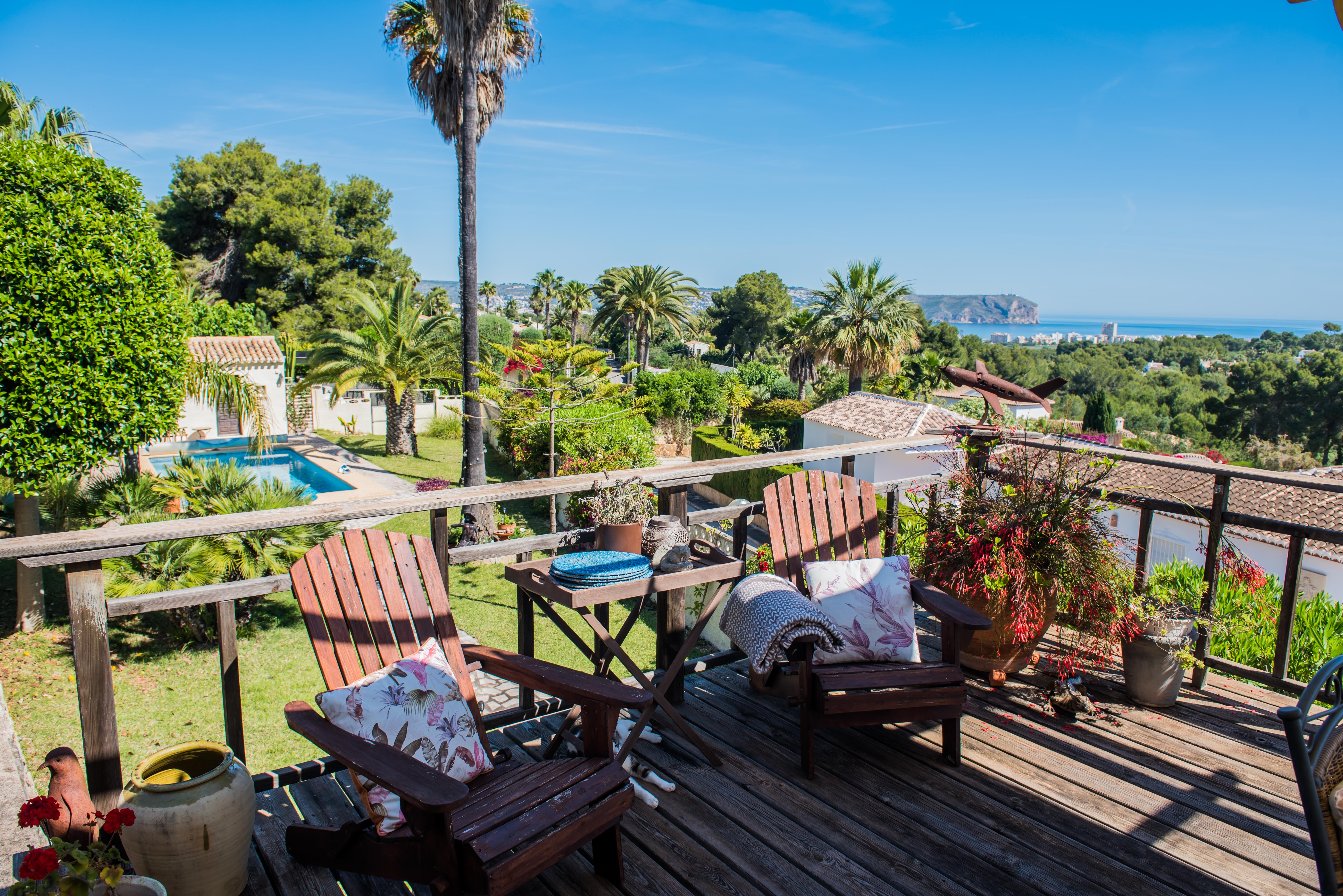 View from the wooden terrace with Adirondack chairs, gardens, and panoramic sea views in Jávea. View from the wooden terrace with Adirondack chairs, gardens, and panoramic sea views in Jávea.