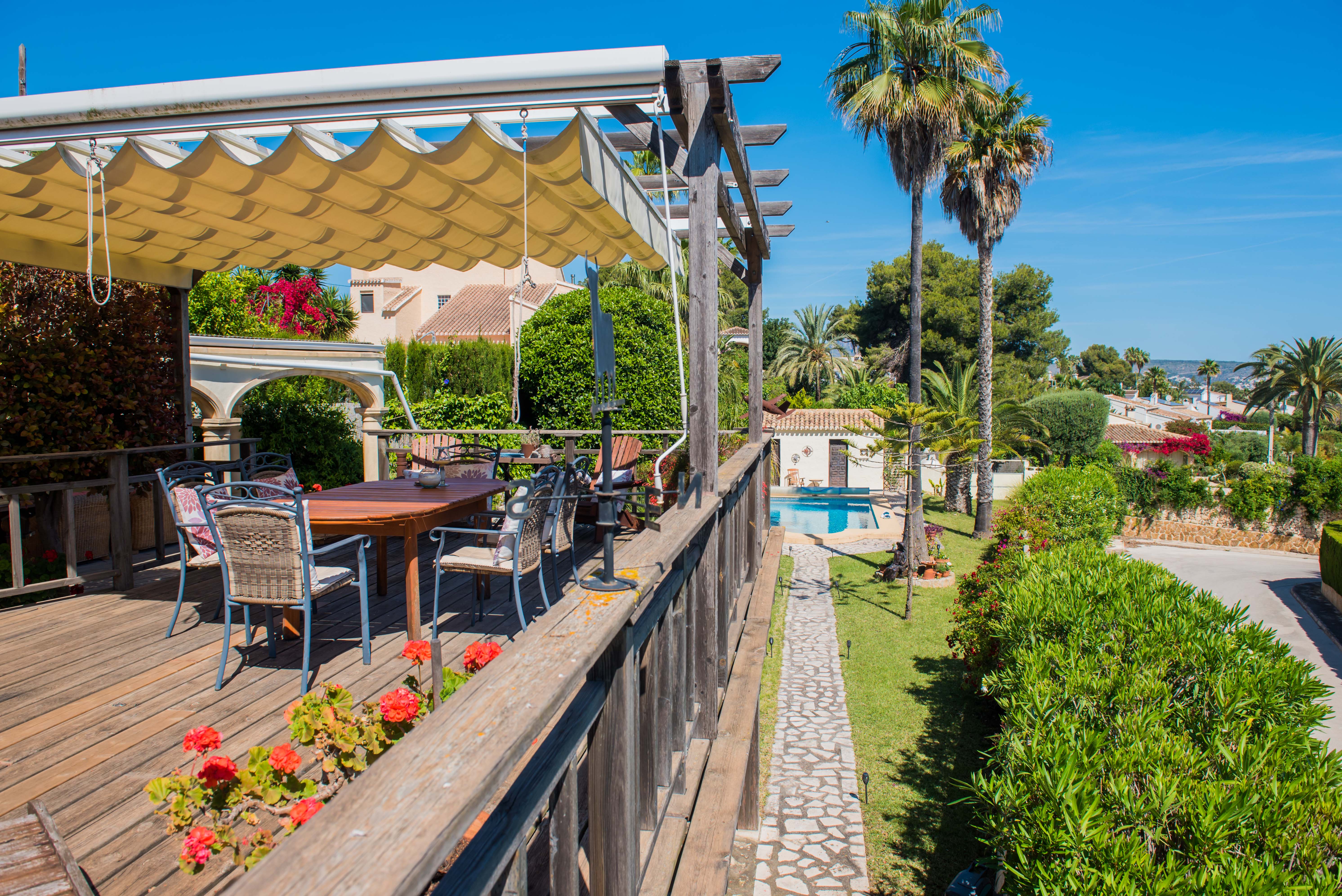 View from the wooden terrace with awning, table, and chairs towards the pool and gardens. View from the wooden terrace with awning, table, and chairs towards the pool and gardens.
