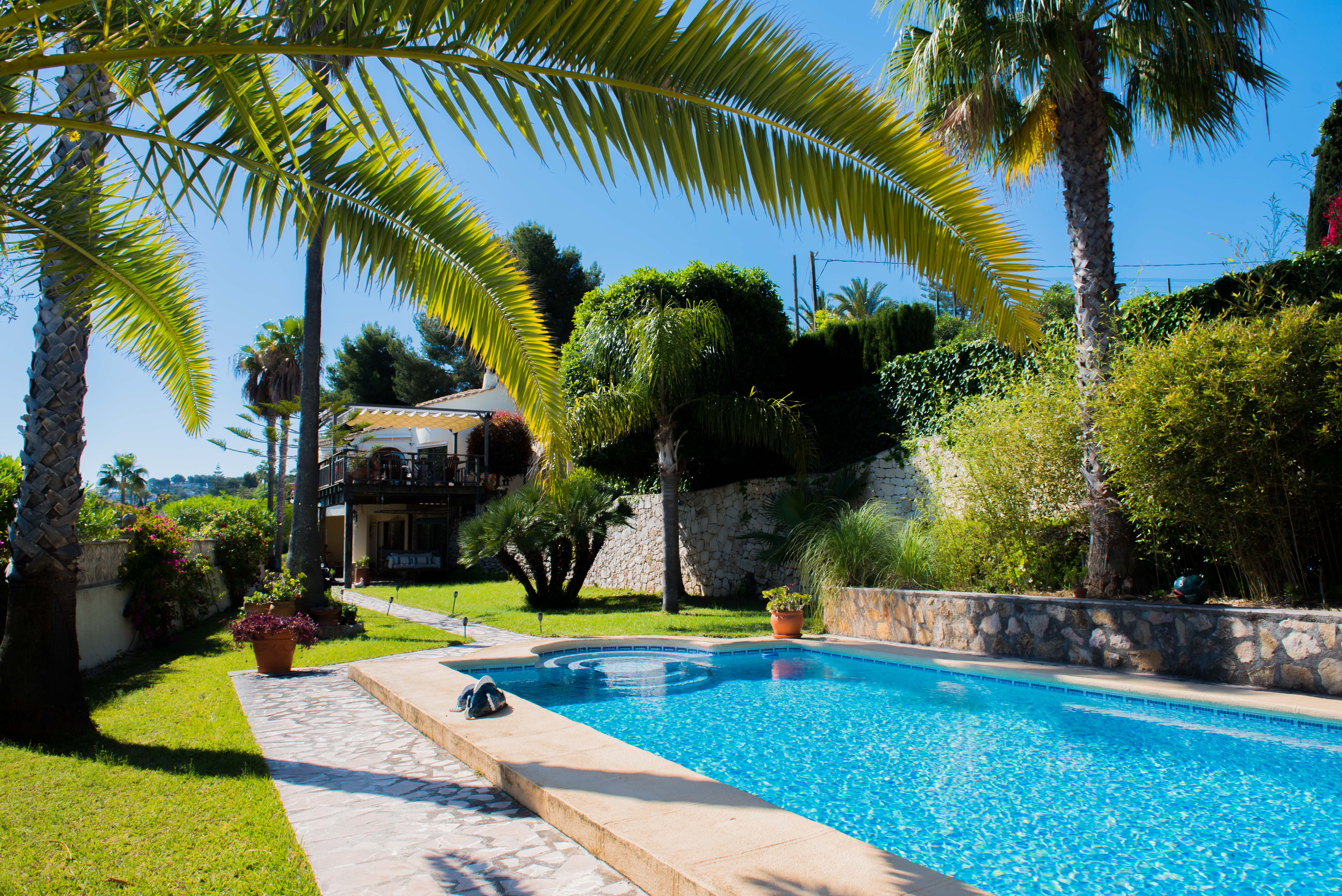 View of the blue-tiled pool and Mediterranean garden with palm trees in Jávea. View of the blue-tiled pool and Mediterranean garden with palm trees in Jávea.