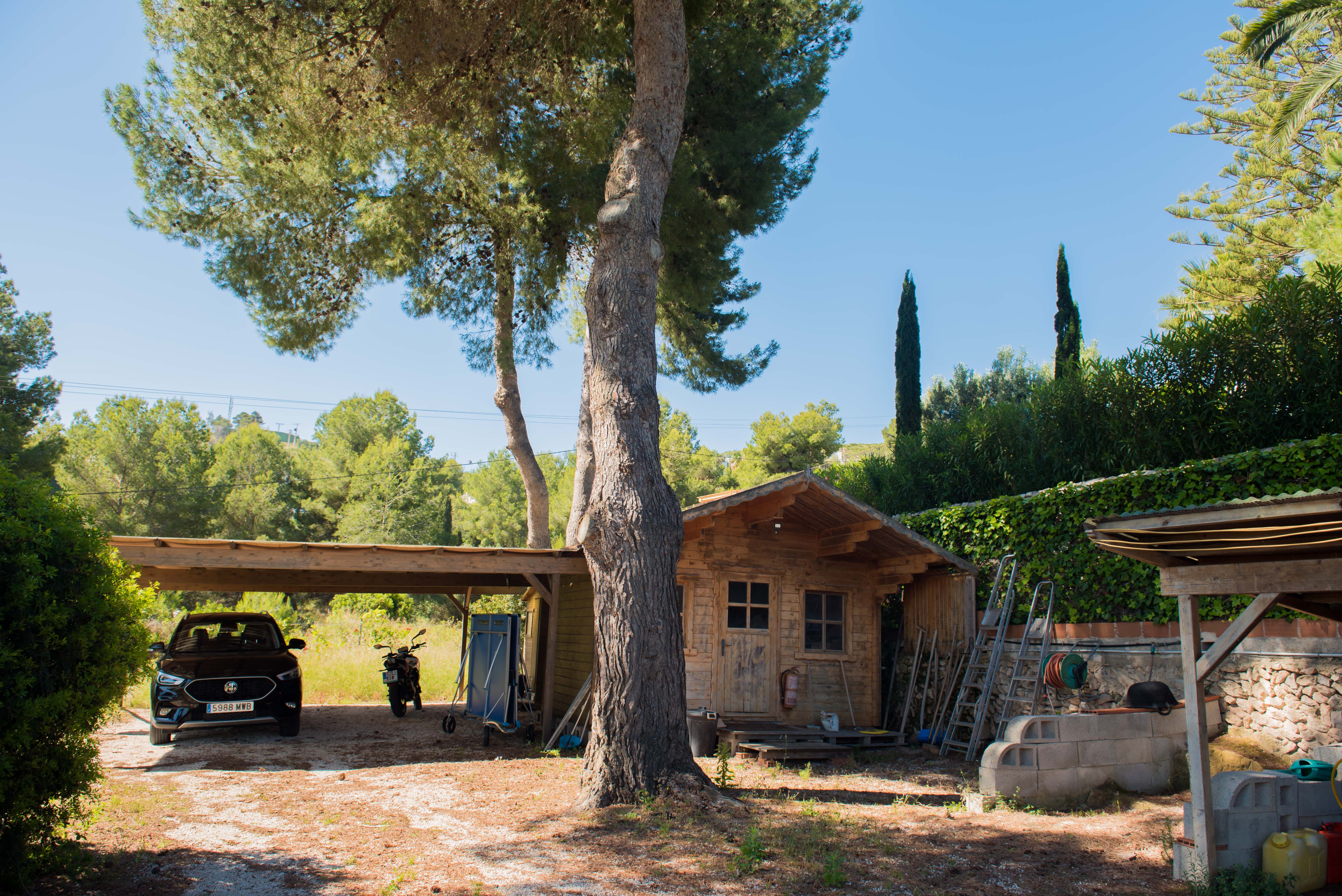 View of the wooden shed and covered garage, surrounded by Mediterranean vegetation and a clear sky. View of the wooden shed and covered garage, surrounded by Mediterranean vegetation and a clear sky.