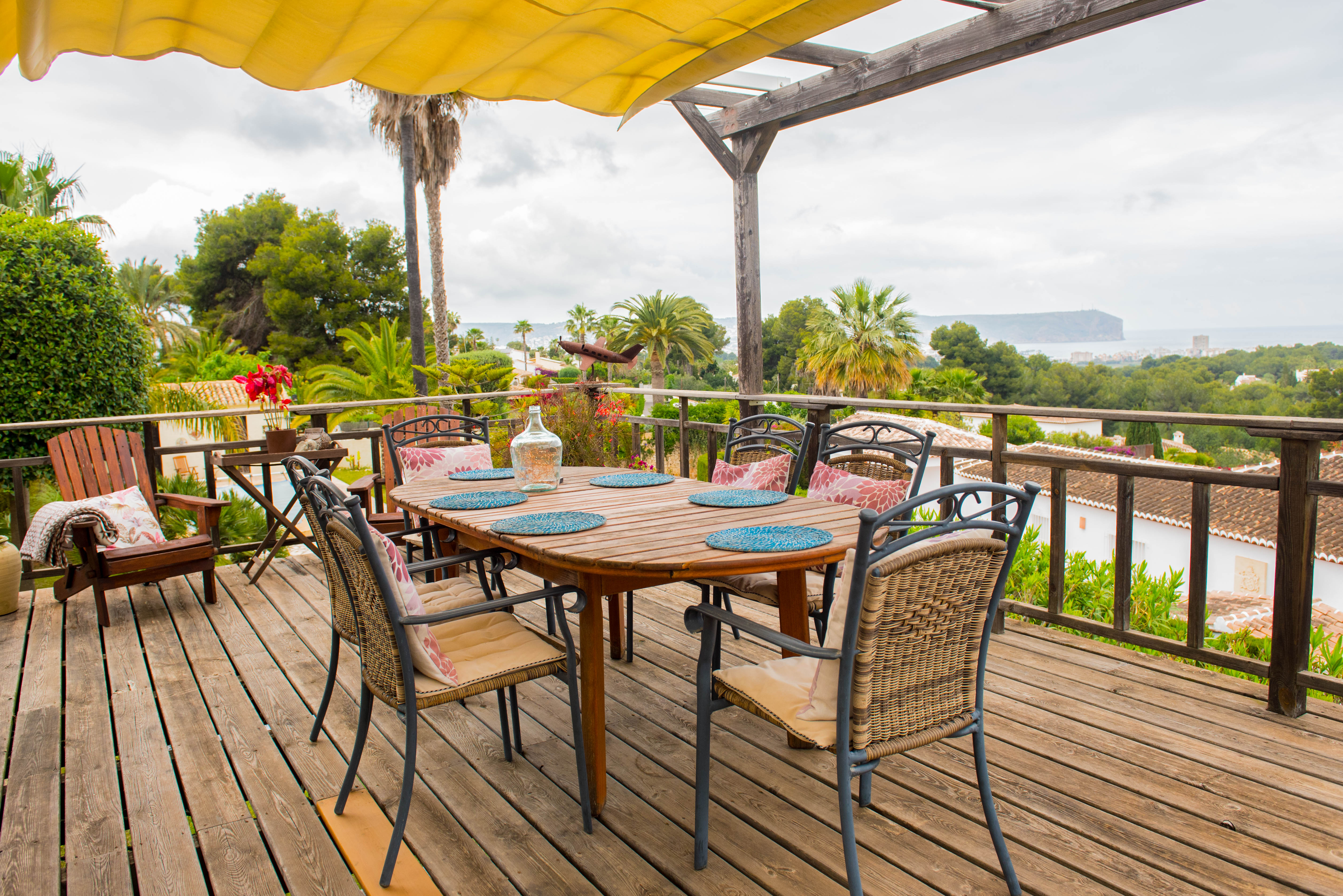 Wooden deck terrace with a retractable yellow awning, featuring an outdoor dining set and panoramic views of the Mediterranean coastline.