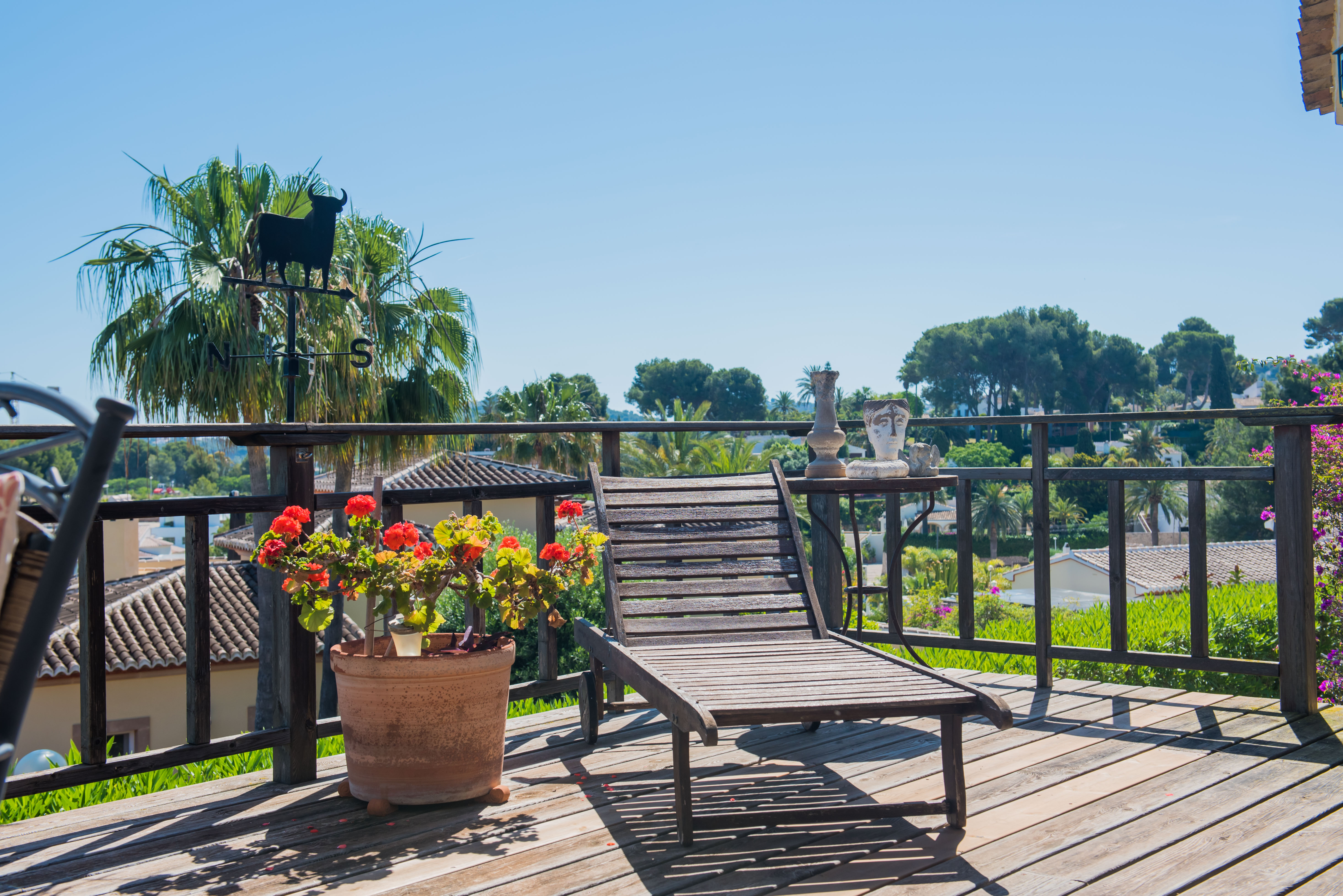 Wooden terrace with a sun lounger, garden views, and decorative details like a bull weathervane and geranium pots. Wooden terrace with a sun lounger, garden views, and decorative details like a bull weathervane and geranium pots.