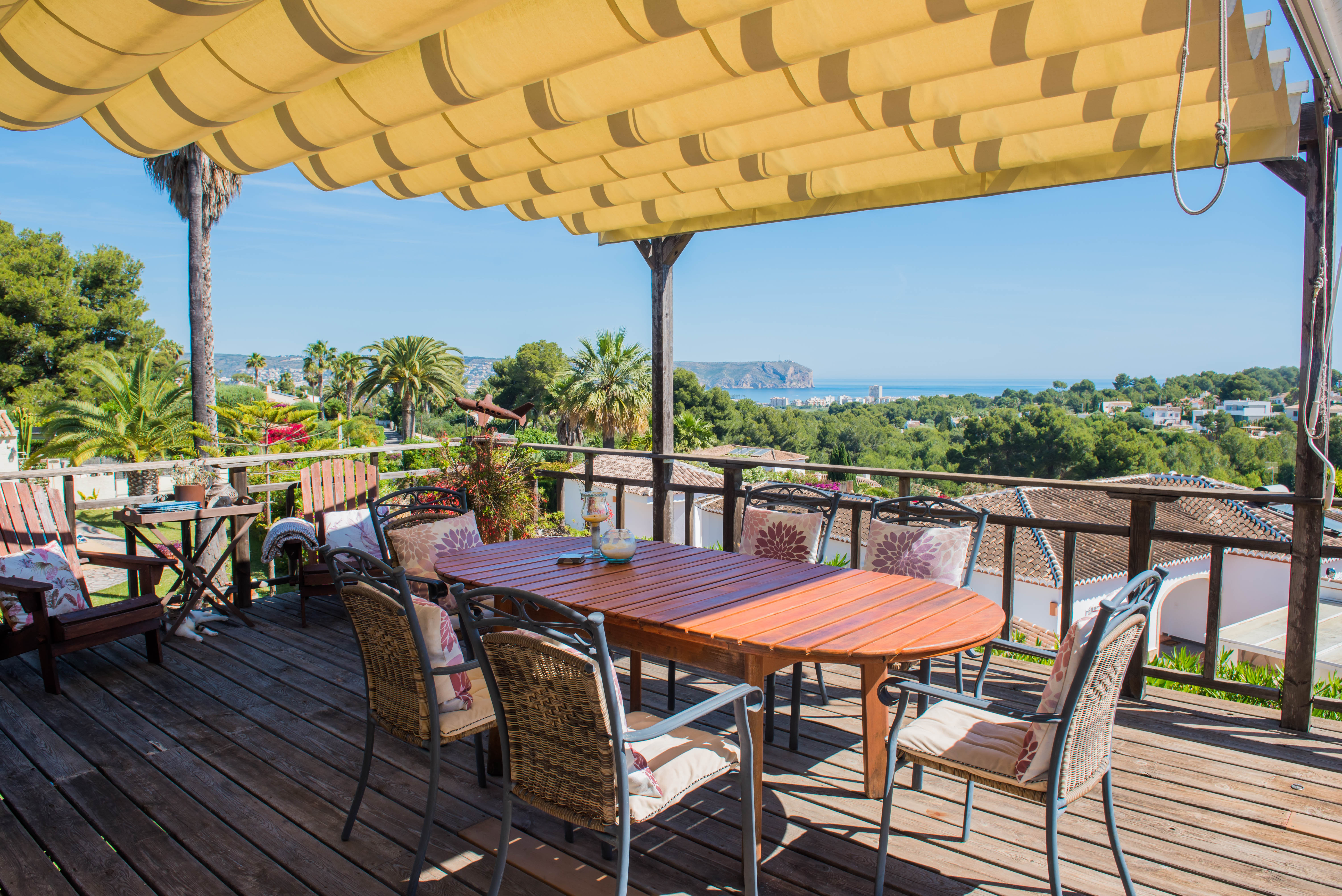 Wooden terrace with awning and dining table, overlooking the sea and lush greenery. Wooden terrace with awning and dining table, overlooking the sea and lush greenery.