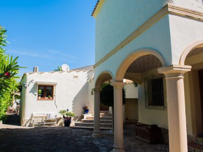 Exterior view of the villa with stone arches and white textured walls, surrounded by Mediterranean greenery.