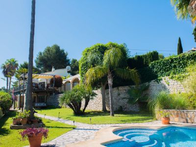 Garden view with a blue mosaic pool and a stone path leading to the Mediterranean-style villa.
