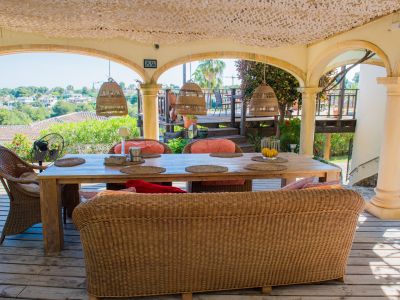 Porch with rustic wood table and wicker seating, illuminated by wicker pendant lamps, overlooking the landscape.