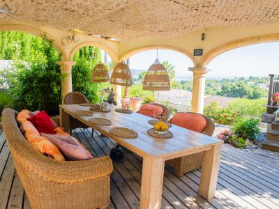 Porch with rustic wood table and wicker seating, offering panoramic views of the garden and the Mediterranean Sea.