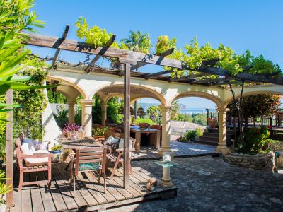 Terrace with a wooden pergola covered in greenery and stone arches overlooking the Mediterranean Sea.