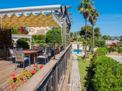 View from the wooden terrace with awning, table, and chairs towards the pool and gardens.