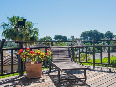 Wooden terrace with a sun lounger, garden views, and decorative details like a bull weathervane and geranium pots.