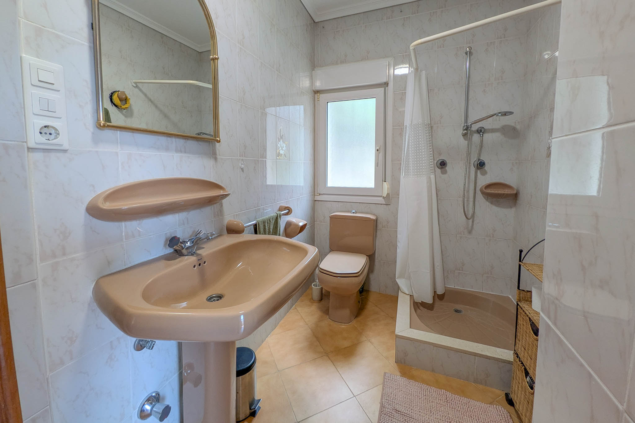 Bathroom featuring beige ceramic fixtures, a walk-in shower with curtain, fully tiled walls, and a window for natural ventilation and light.