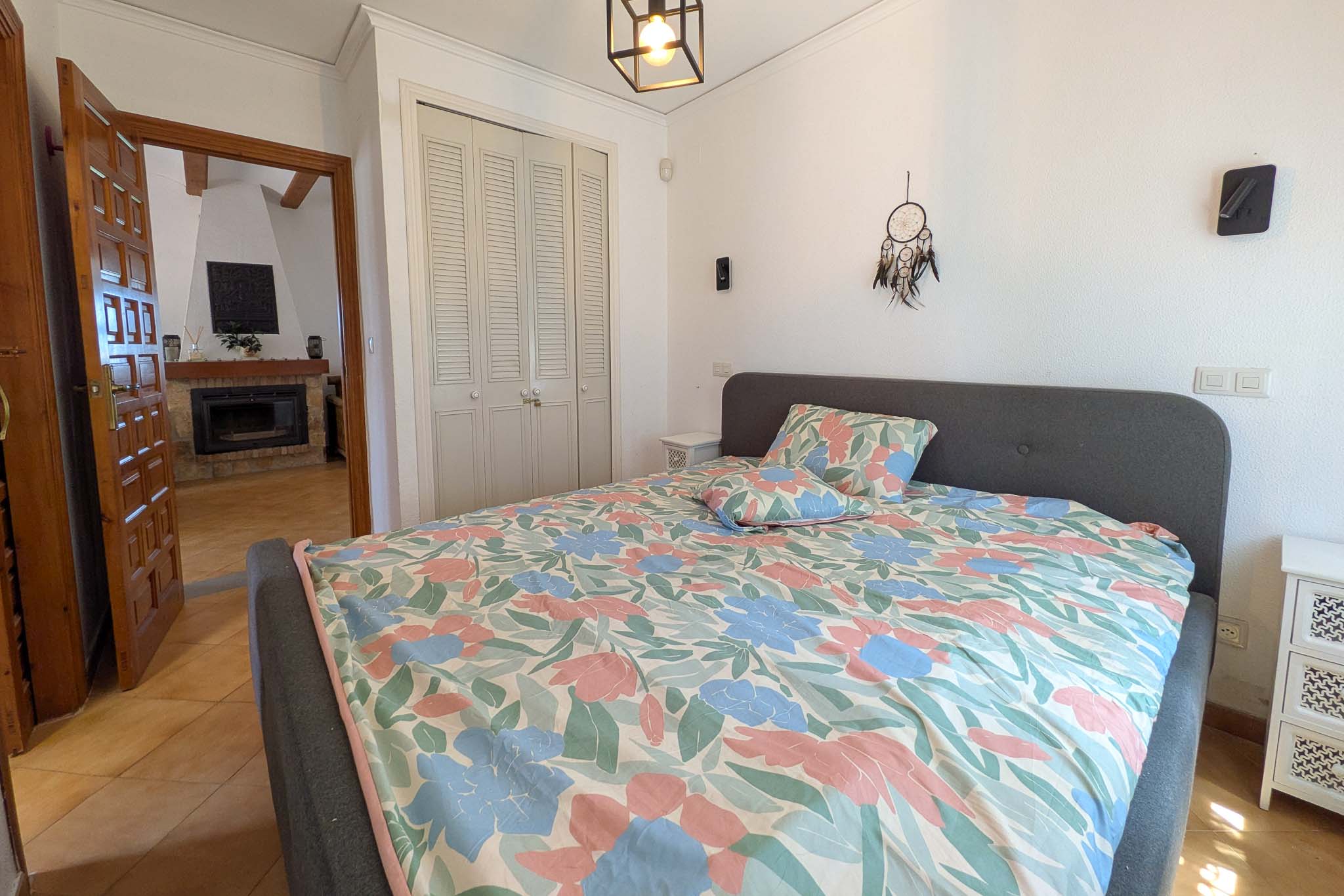 Bedroom featuring built-in wardrobes with white louvered doors and a view toward the living area's stone fireplace through a classic wooden door.