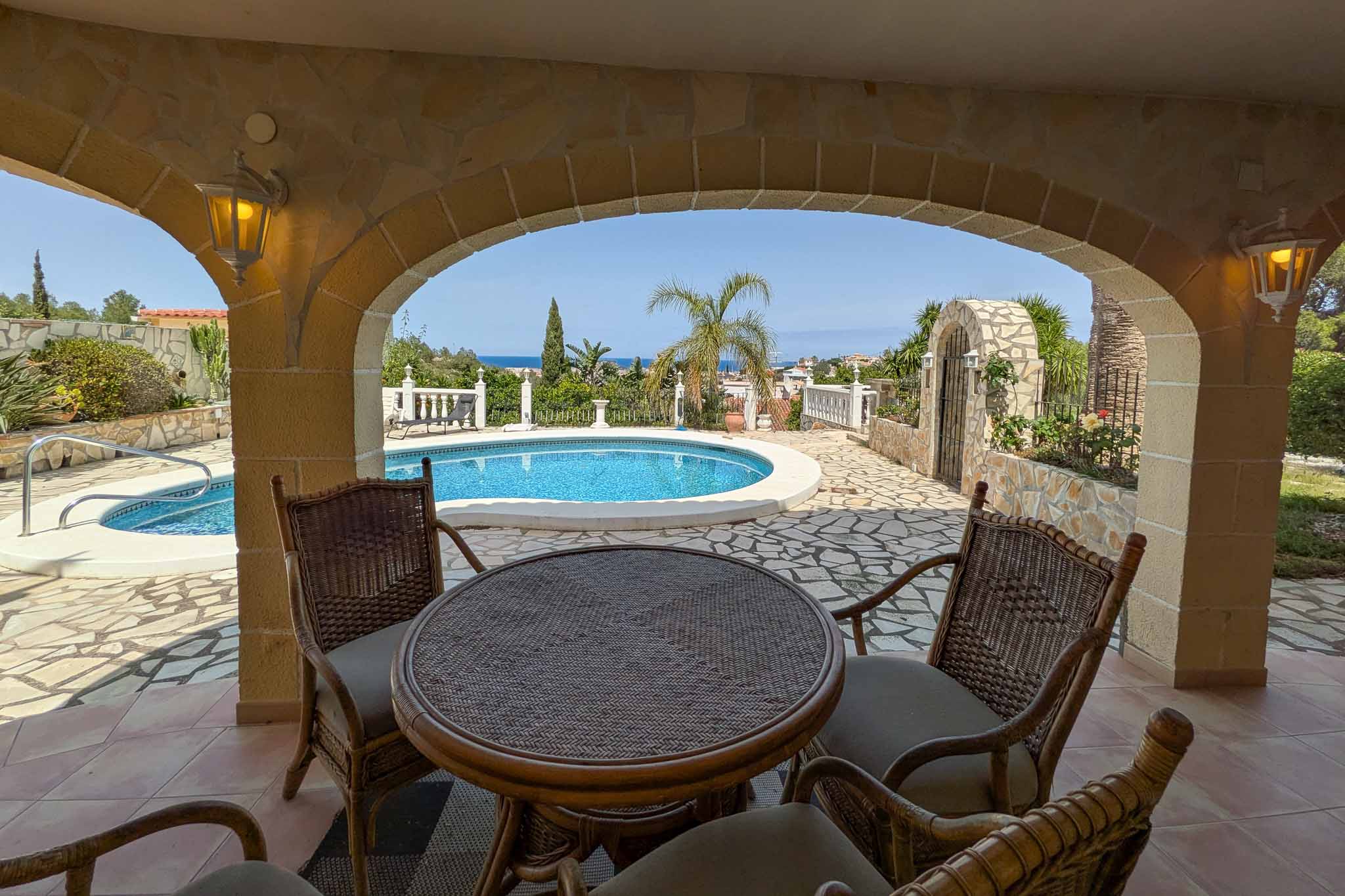Covered terrace featuring natural stone arches and wicker seating, overlooking the private pool and the Mediterranean coastline.