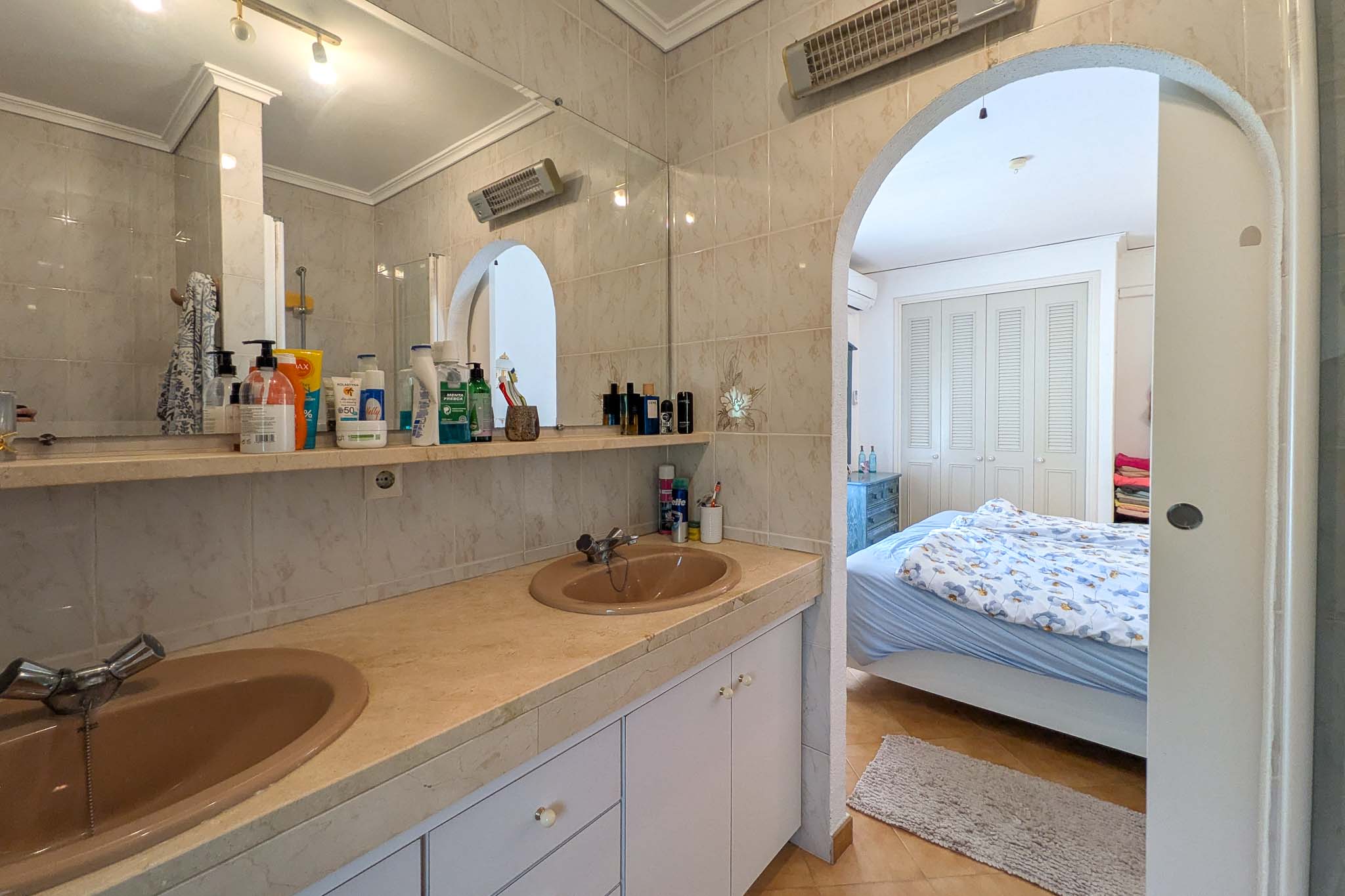 En-suite bathroom featuring a double vanity with marble countertop and an arched entrance leading to the main bedroom.