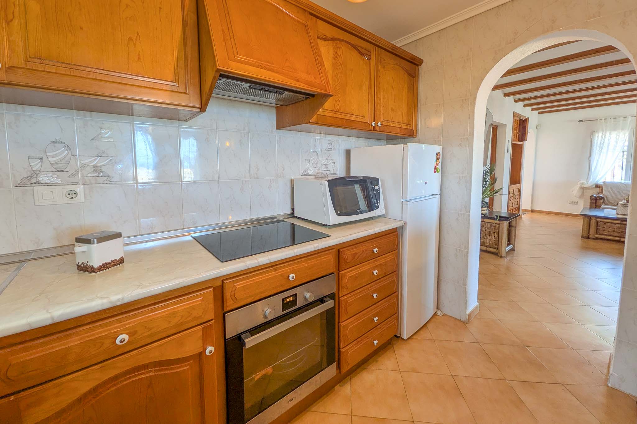 Equipped kitchen featuring classic wood cabinetry, marble-effect countertops, and integrated appliances, opening into the living area via a traditional archway.