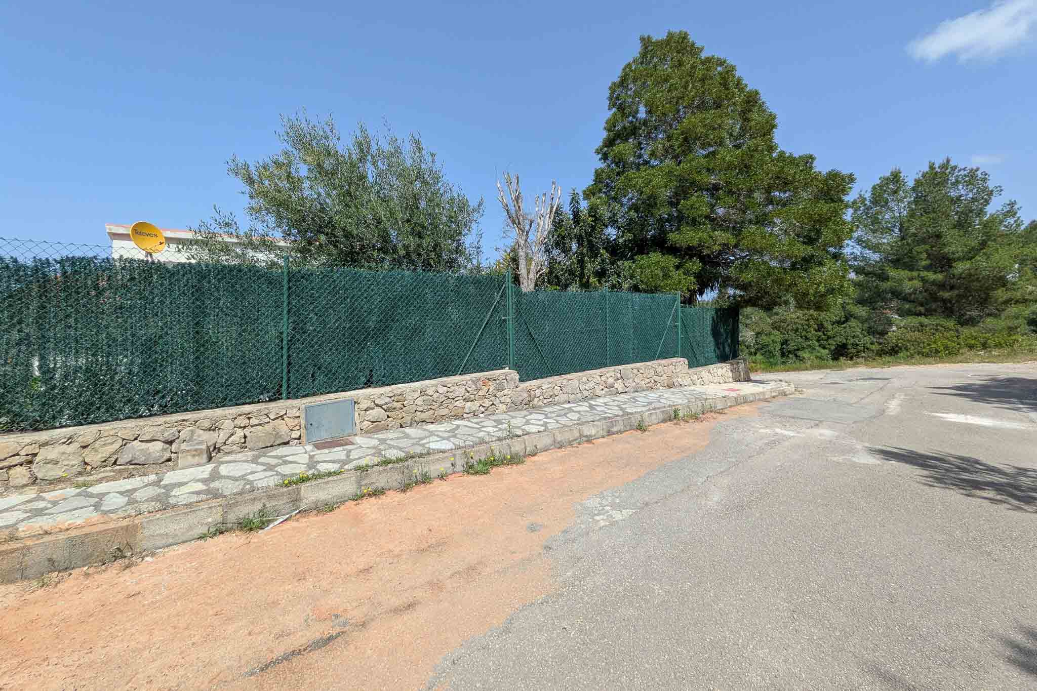 Exterior boundary featuring a natural stone wall, green privacy fencing, and a stone-paved sidewalk along a quiet residential street.