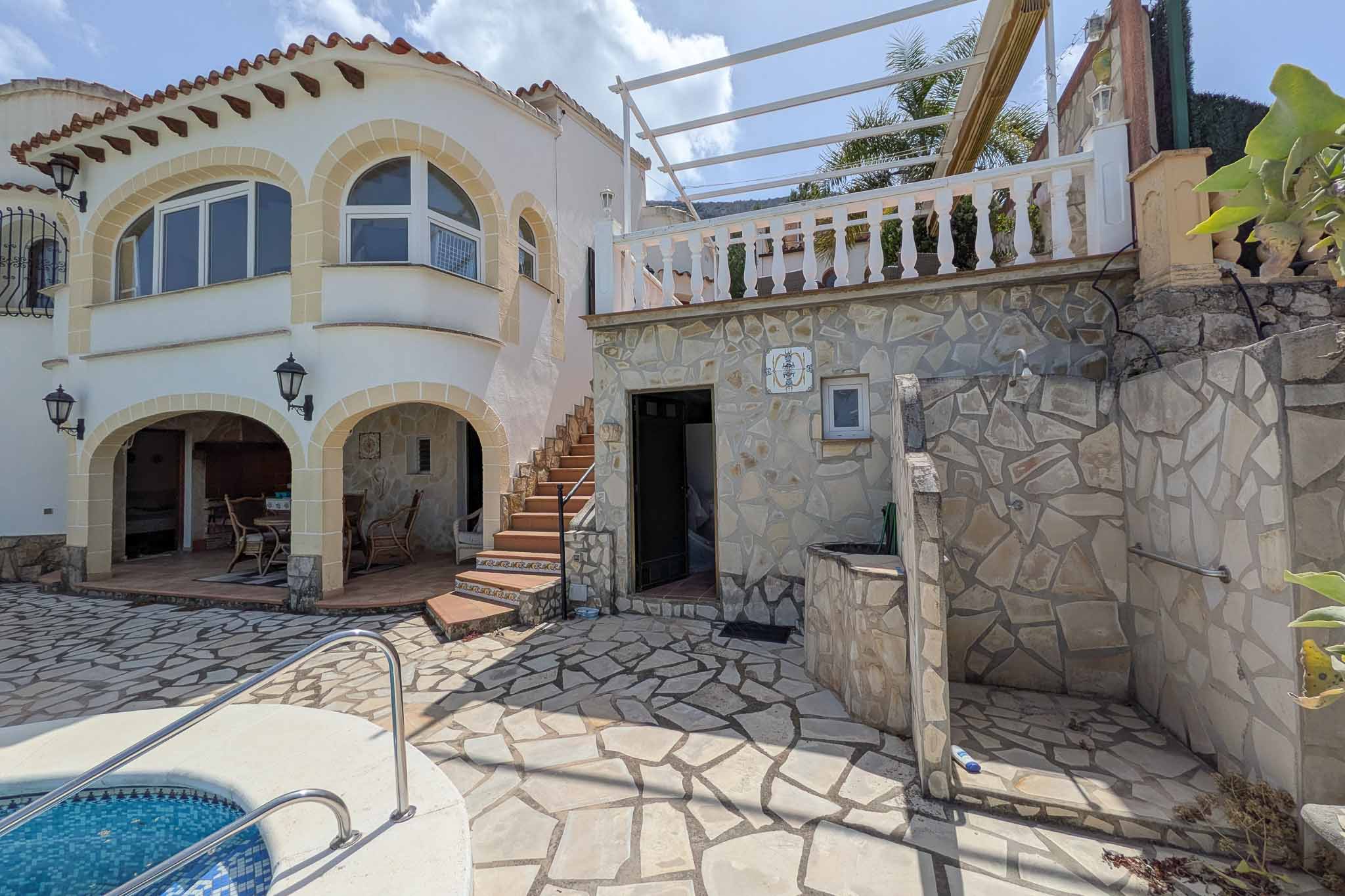 Exterior stone-paved terrace featuring an integrated outdoor shower, pool access, and stairs leading to an upper level with a white balustrade.