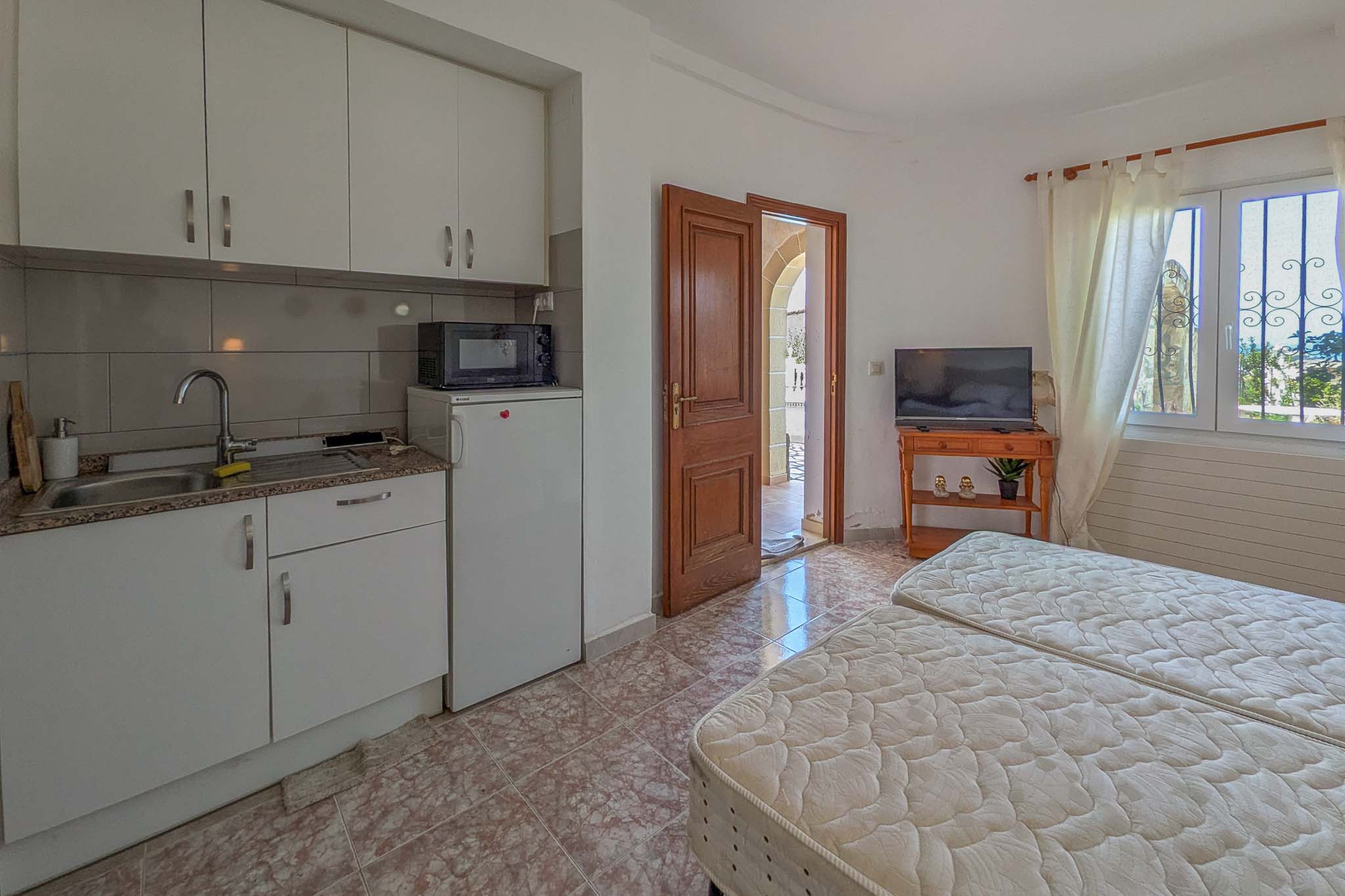 Independent ground-floor apartment featuring a compact kitchenette, two single beds, and direct access to the terrace through a classic wooden door.