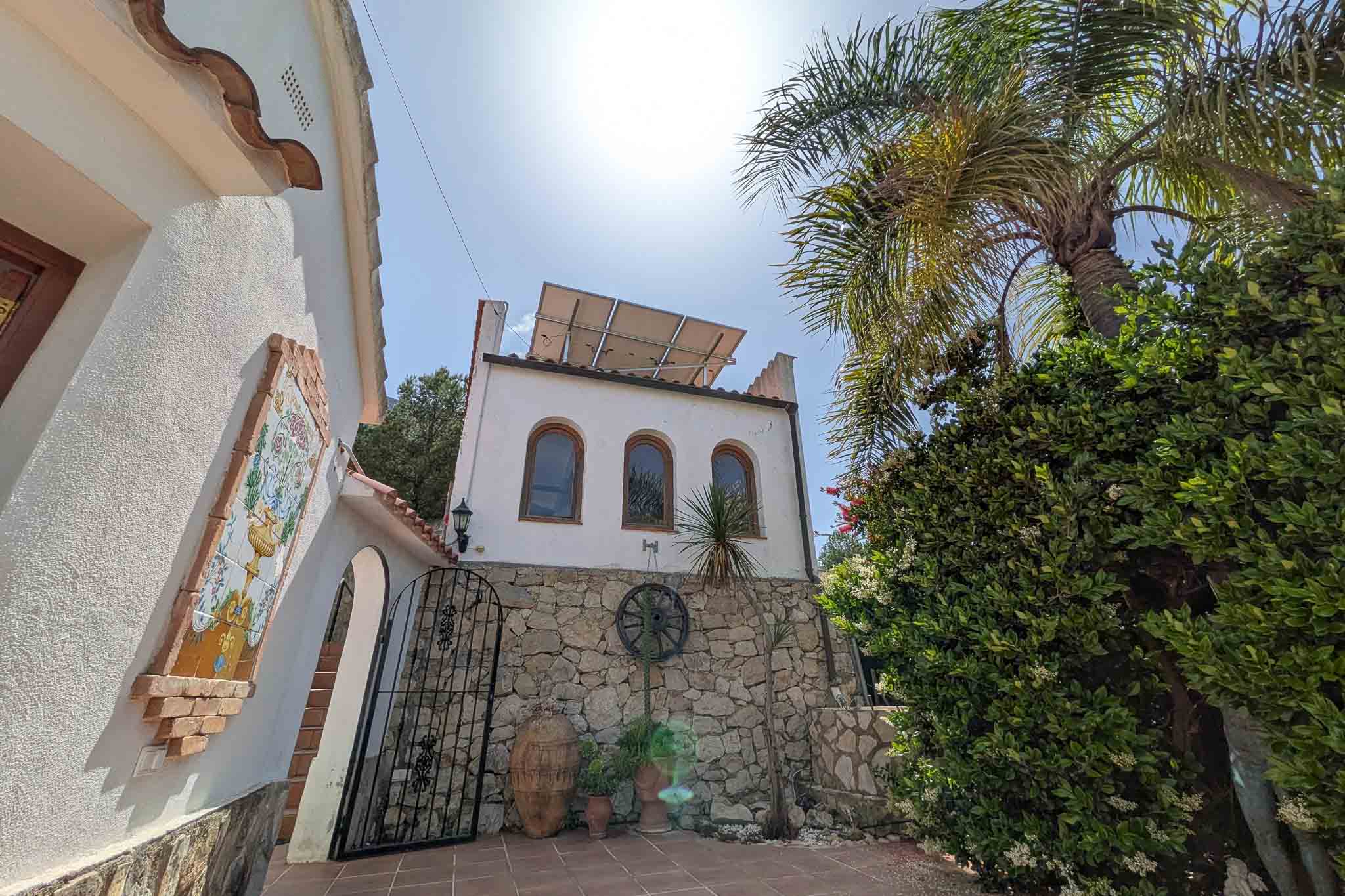 Mediterranean facade featuring natural stone walls, rooftop solar panels, and traditional decorative elements like a ceramic mural and wrought iron gate.