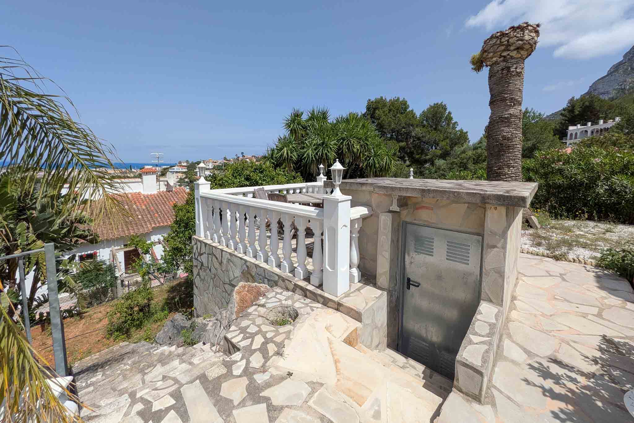 Outdoor terrace featuring white balustrades and natural stone paving, offering clear sea views and access to a technical storage area.