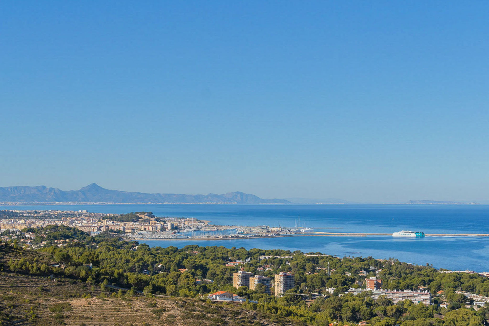 Panoramic view from the property overlooking Dénia's port and the Mediterranean Sea, featuring the ferry terminal and distant mountain ranges.