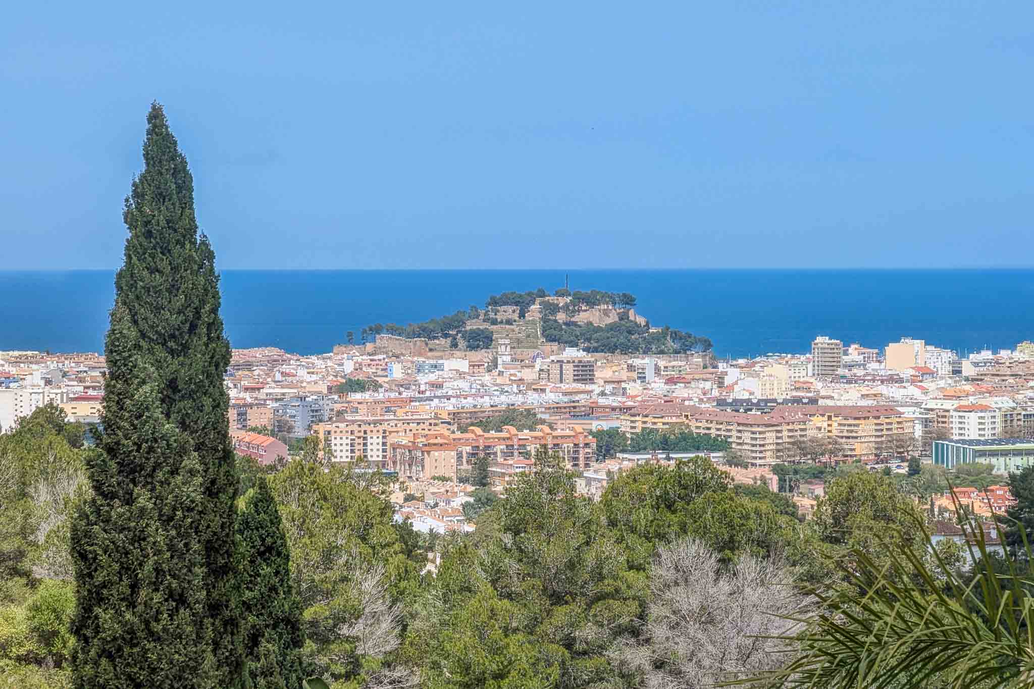 Panoramic views from the property overlooking Dénia castle and the Mediterranean Sea, framed by lush local vegetation and cypress trees.
