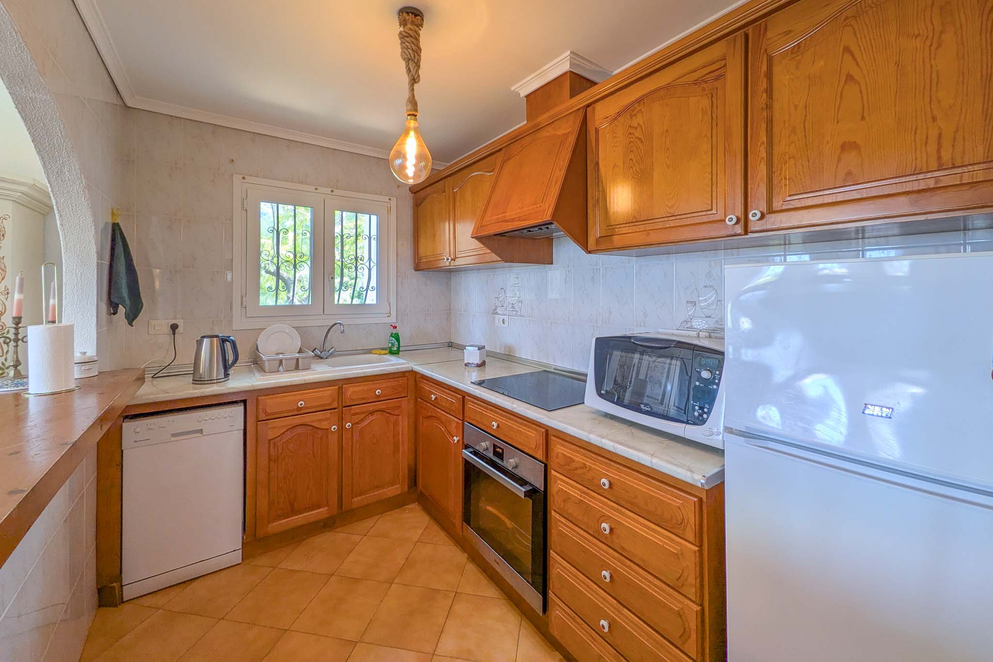 Rustic-style kitchen featuring wood cabinetry, marble countertops, and integrated appliances. It includes a unique rope pendant light and natural light from the window.