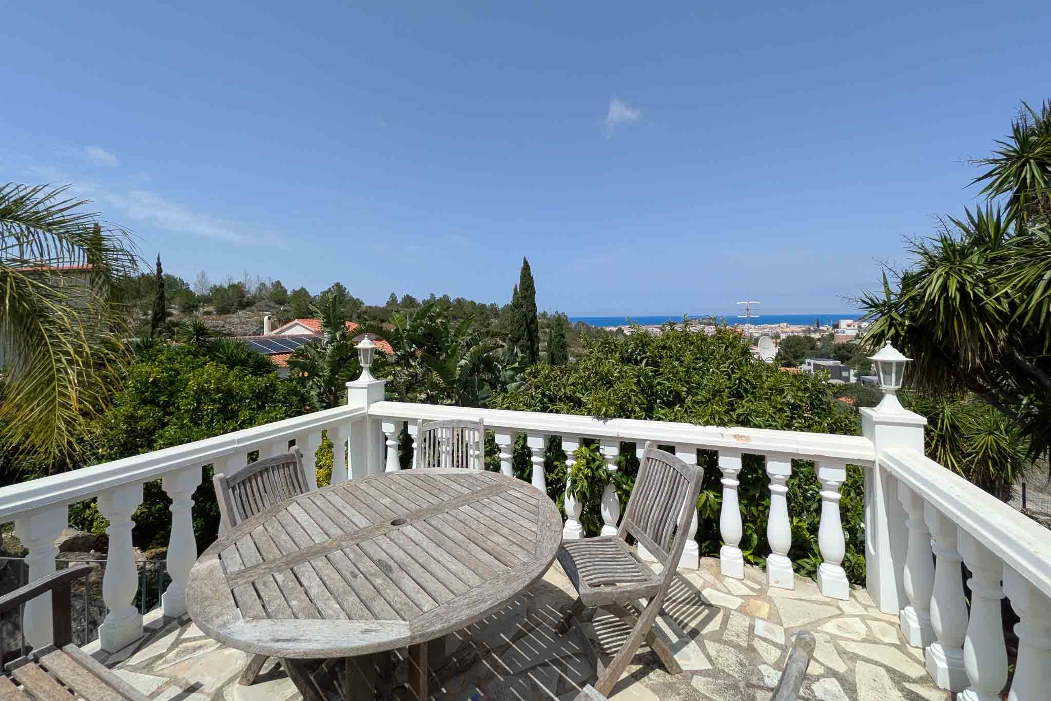 Terrace with white balustrade and wooden furniture on irregular stone flooring, offering clear views of the Mediterranean Sea and the town of Dénia.