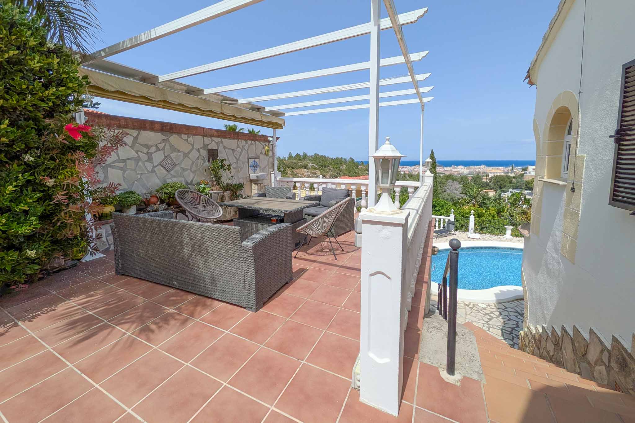Upper terrace featuring an outdoor lounge area, white pergola, and panoramic views of the Mediterranean Sea and Dénia, overlooking the pool area.
