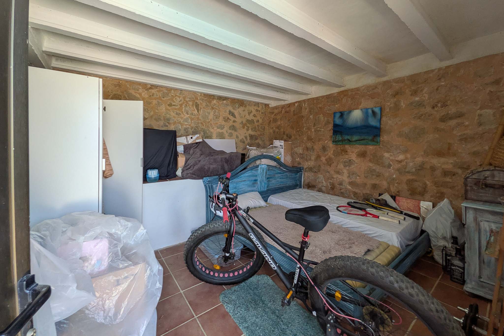 Versatile storage room featuring original exposed stone walls, white beamed ceilings, and traditional terracotta tile flooring.