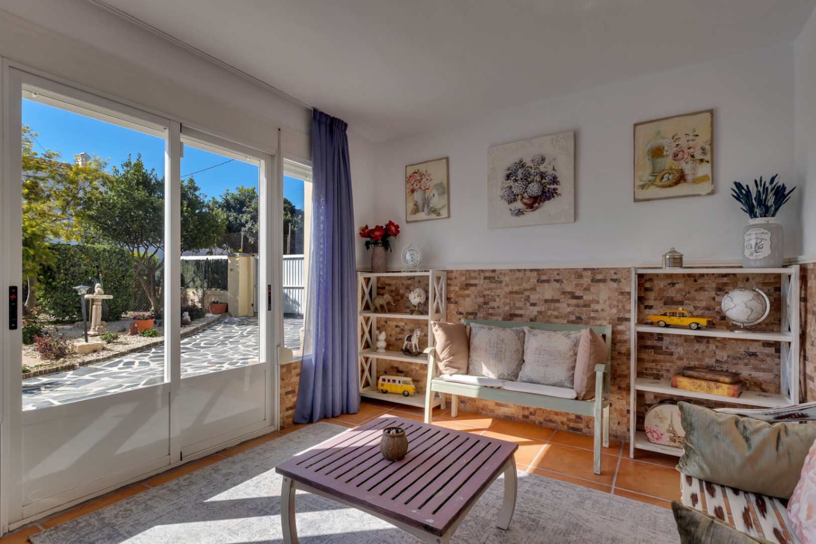 Bright living space featuring terracotta flooring, natural stone wall cladding, and large sliding doors opening onto the paved garden patio.