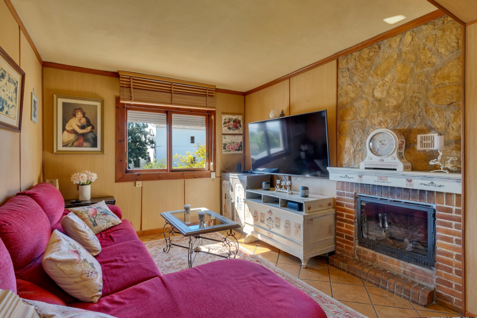 Cozy living area featuring a rustic brick fireplace with stone accents, wood-paneled walls, and a comfortable red sofa.