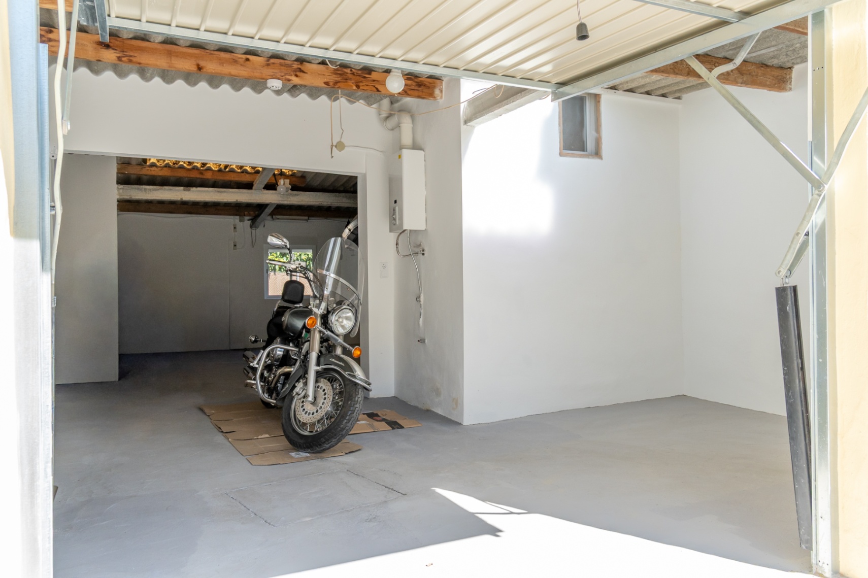 Enclosed garage and parking area featuring concrete flooring, wooden ceiling beams, and a wall-mounted gas boiler, providing ample space for vehicles.