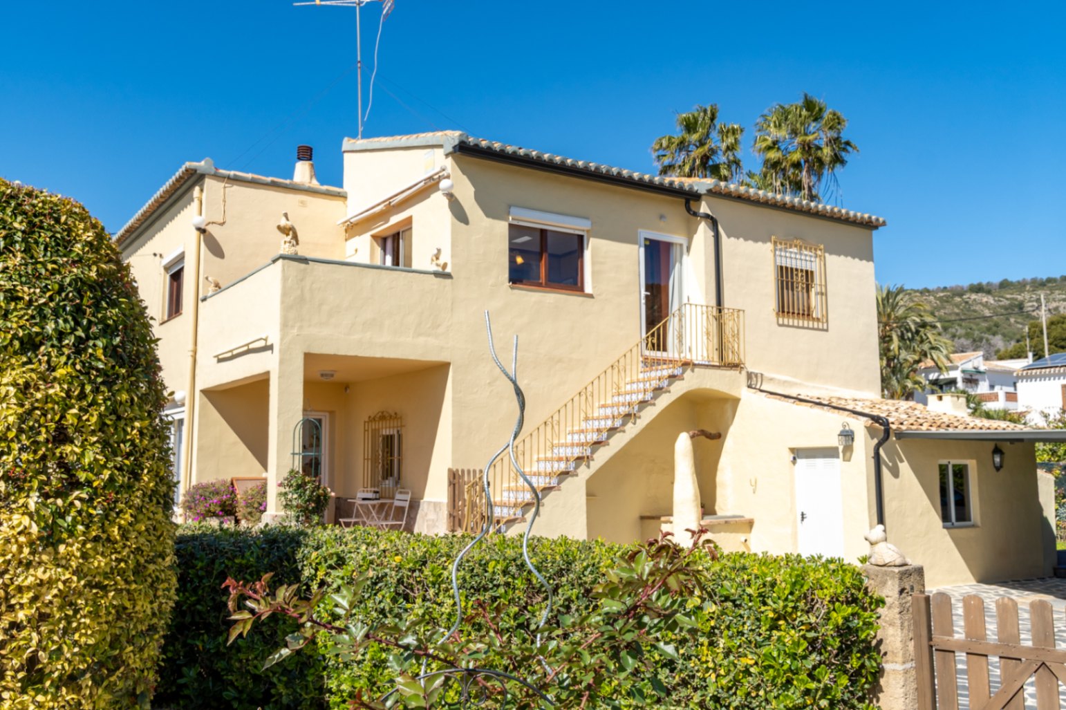 Exterior view of the villa featuring a cream facade, an external staircase with decorative tiling, and multiple terraces overlooking the garden.