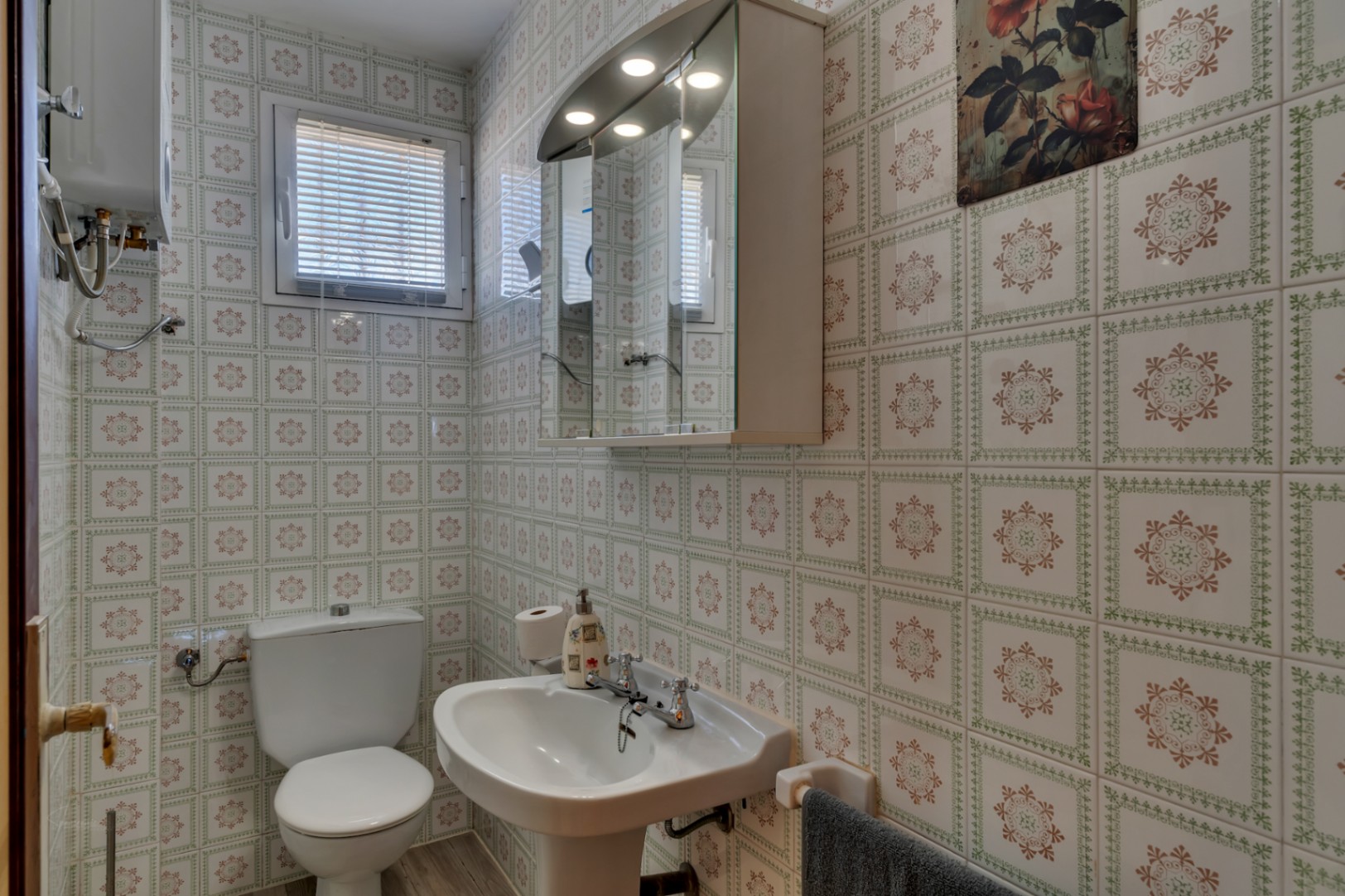 Functional bathroom featuring patterned wall tiles, a pedestal sink, toilet, and a mirrored medicine cabinet with integrated lighting.
