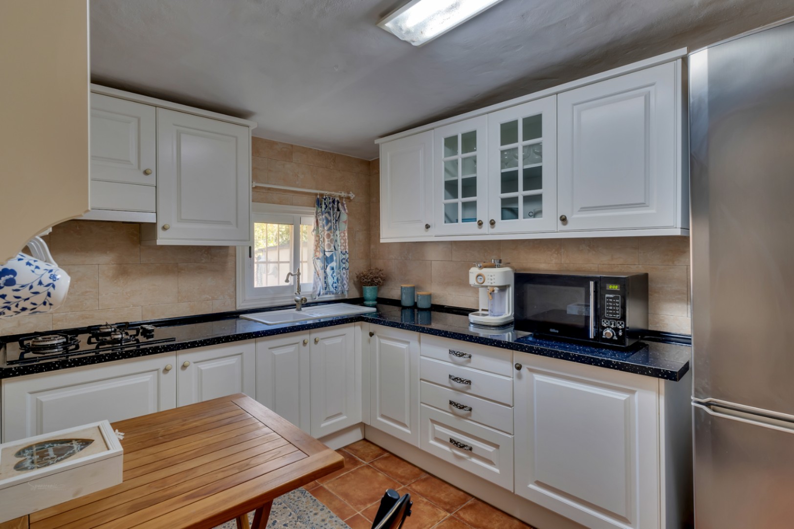Functional kitchen featuring white classic cabinetry, dark speckled countertops, stainless steel appliances, and traditional terracotta floor tiles.