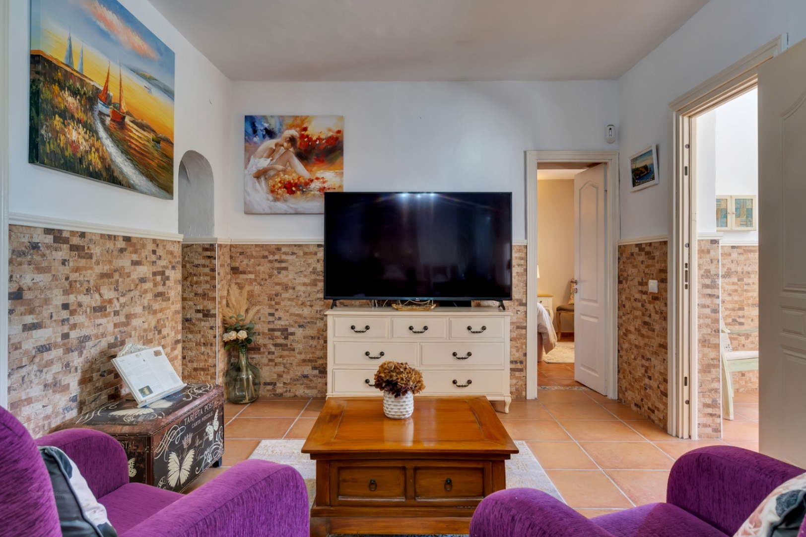 Living area featuring stone-effect wall tiling, terracotta floors, and rustic furniture, providing access to the lower level bedrooms.