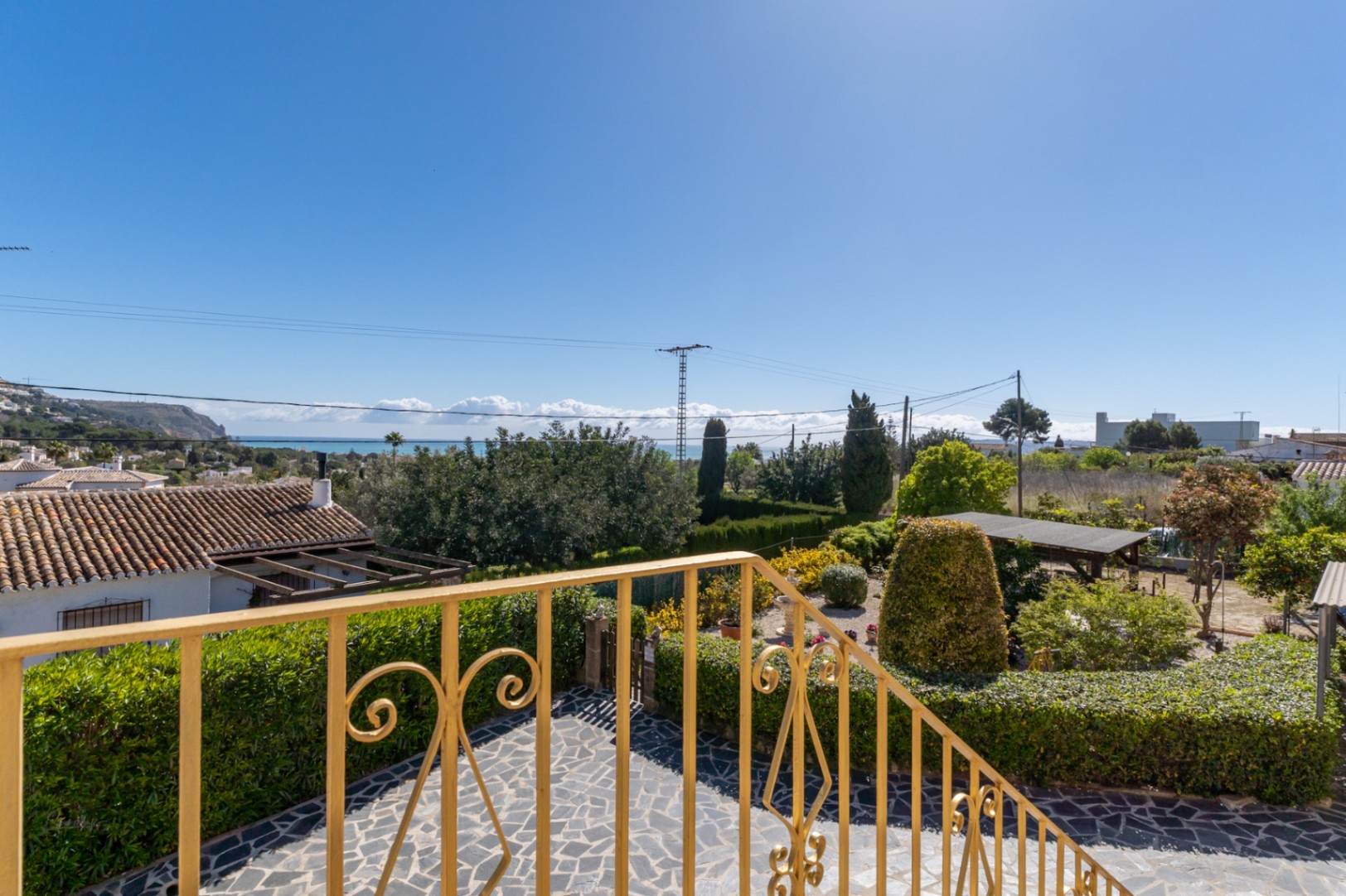Panoramic sea views from the upper terrace, featuring an ornamental yellow railing and a landscaped Mediterranean garden with stone paving.