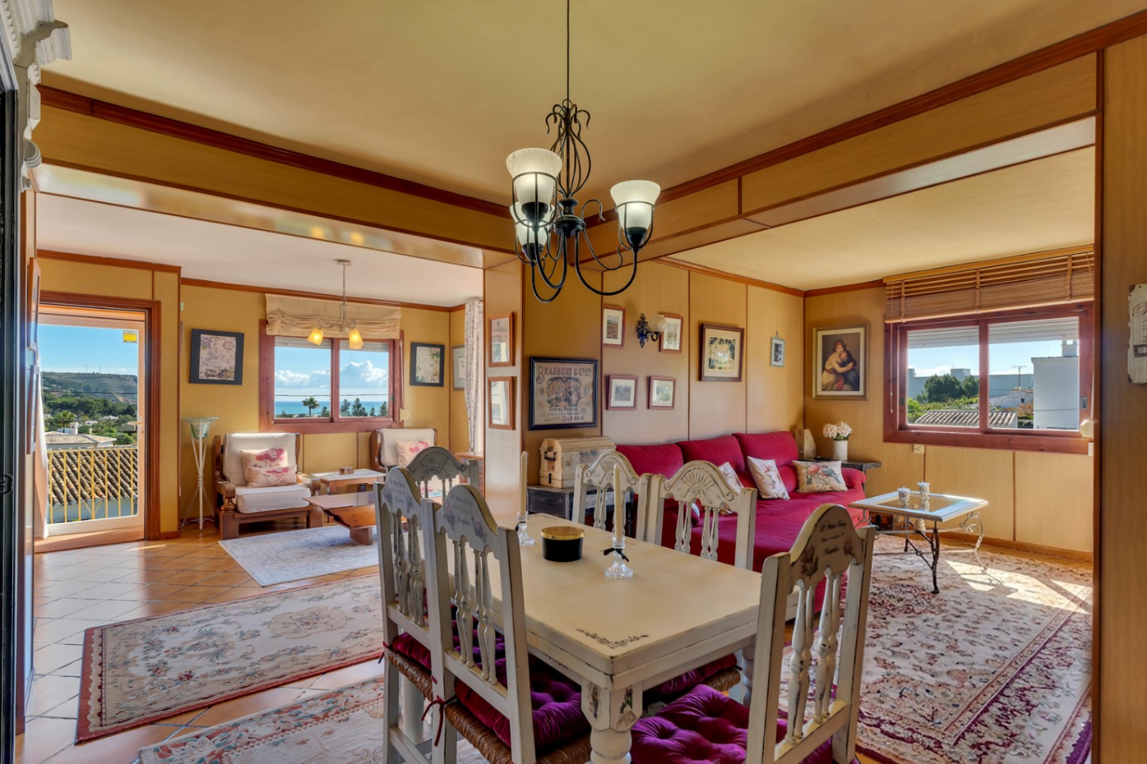Rustic living-dining area featuring wood-paneled walls, traditional furniture, and large windows offering panoramic views of the Mediterranean coastline and sea.
